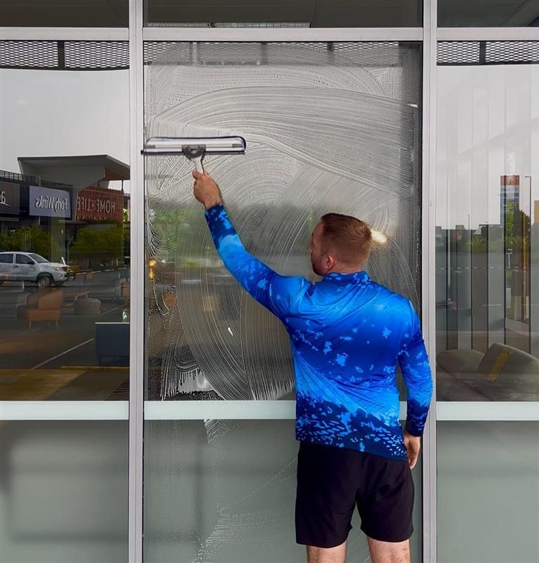 A Man In A Blue Suit Is Using A High Pressure Washer To Clean A Driveway — Pristine and Co In Coomera, QLD