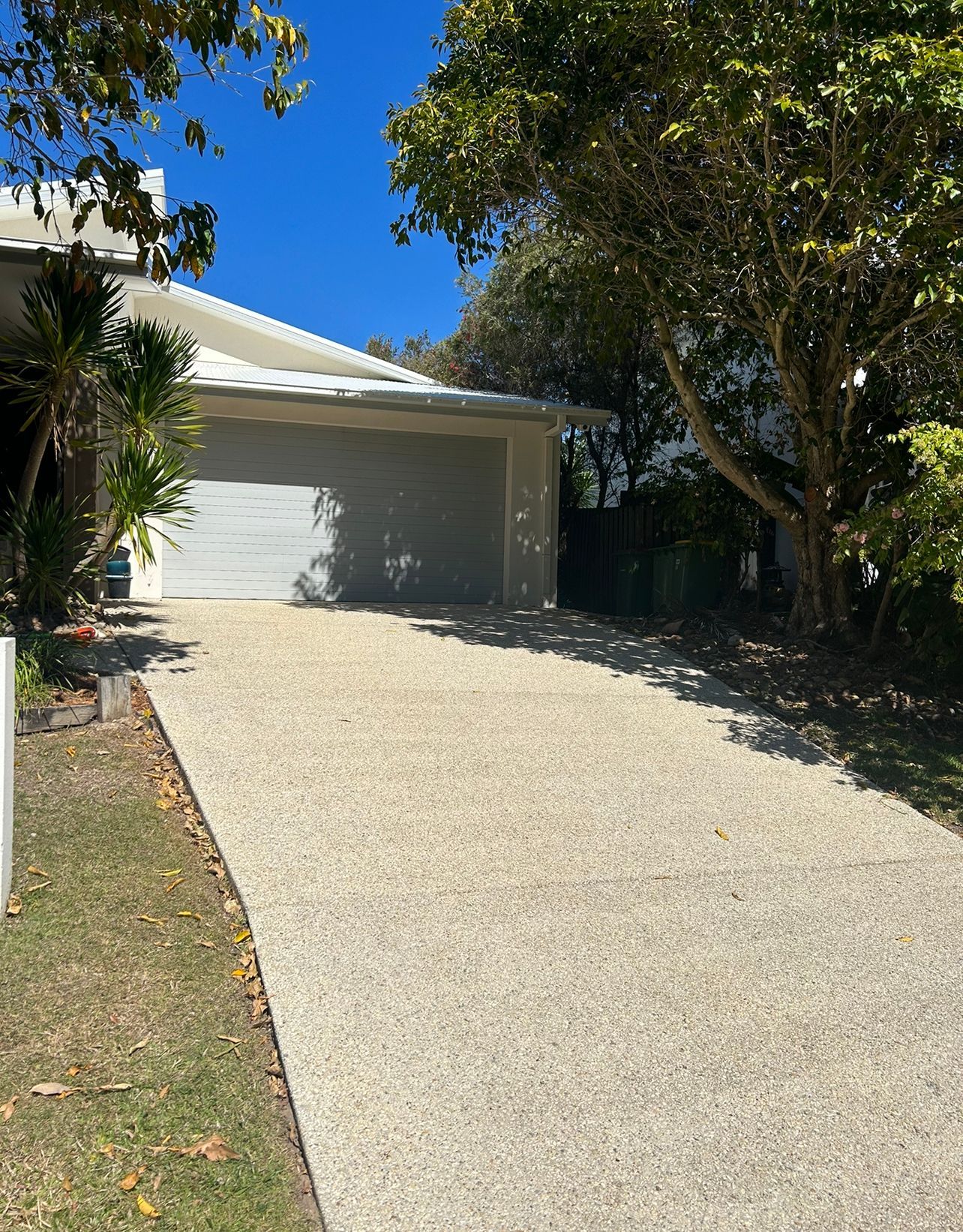 A Man In A Blue Suit Is Using A High Pressure Washer To Clean A Driveway — Pristine and Co In Coomera, QLD