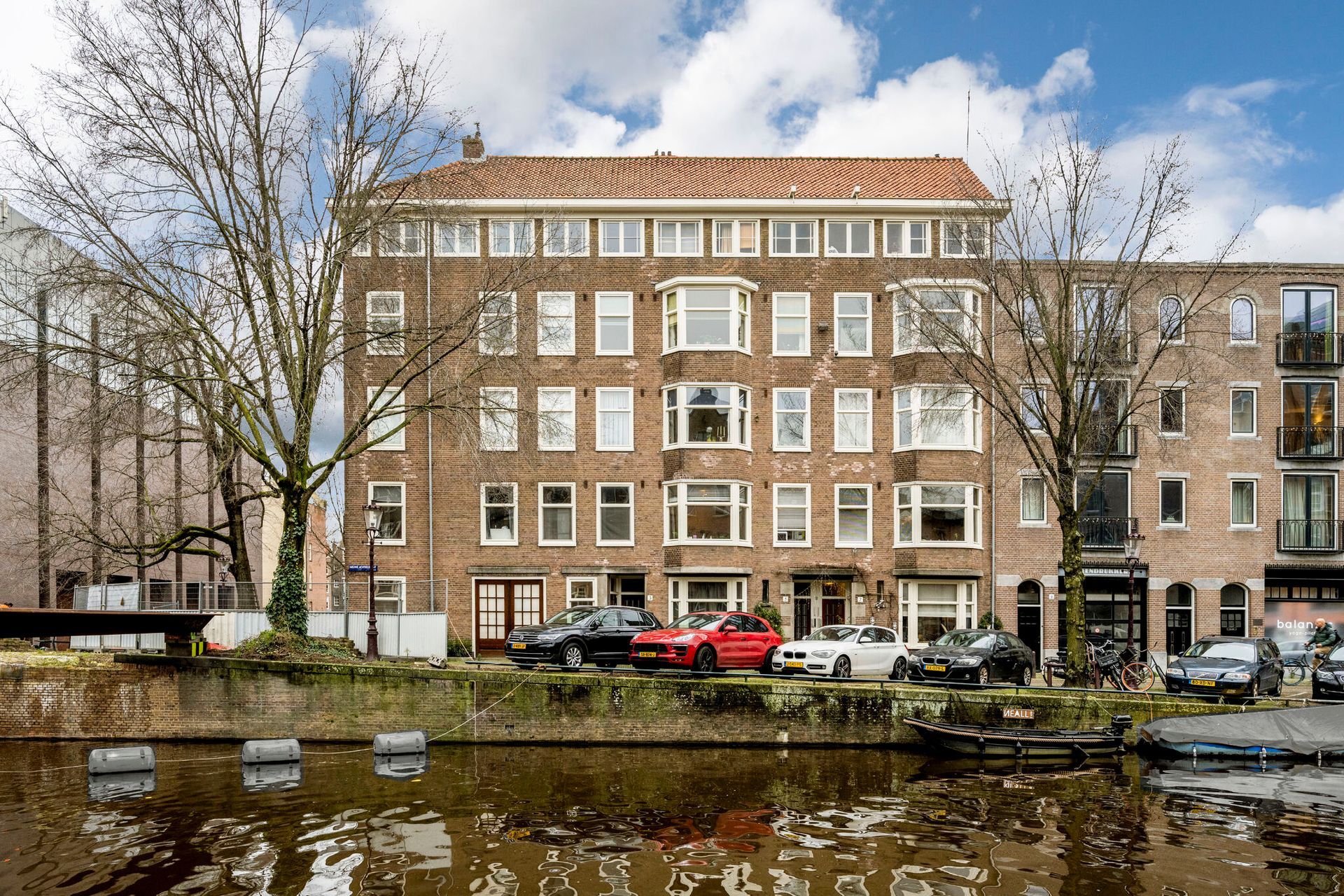 Nieuwe Achtergracht Amsterdam. een groot gebouw met auto's ervoor geparkeerd naast een rivier.