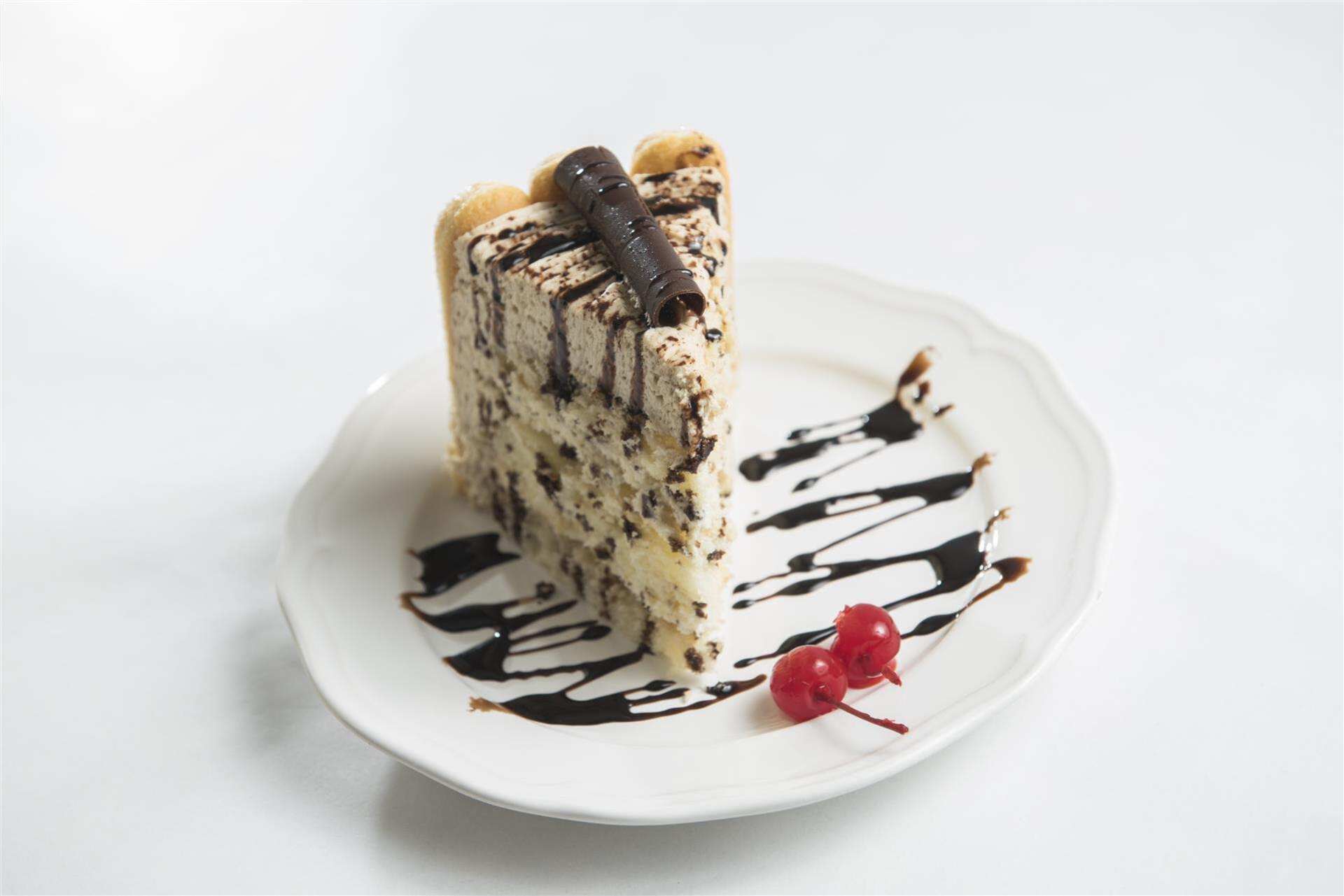 Mousse cake topped with chocolate on a white plate with cherries