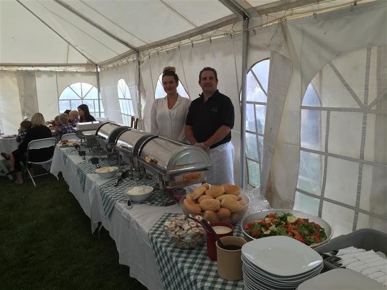 two people standing behind a catering table in a tent