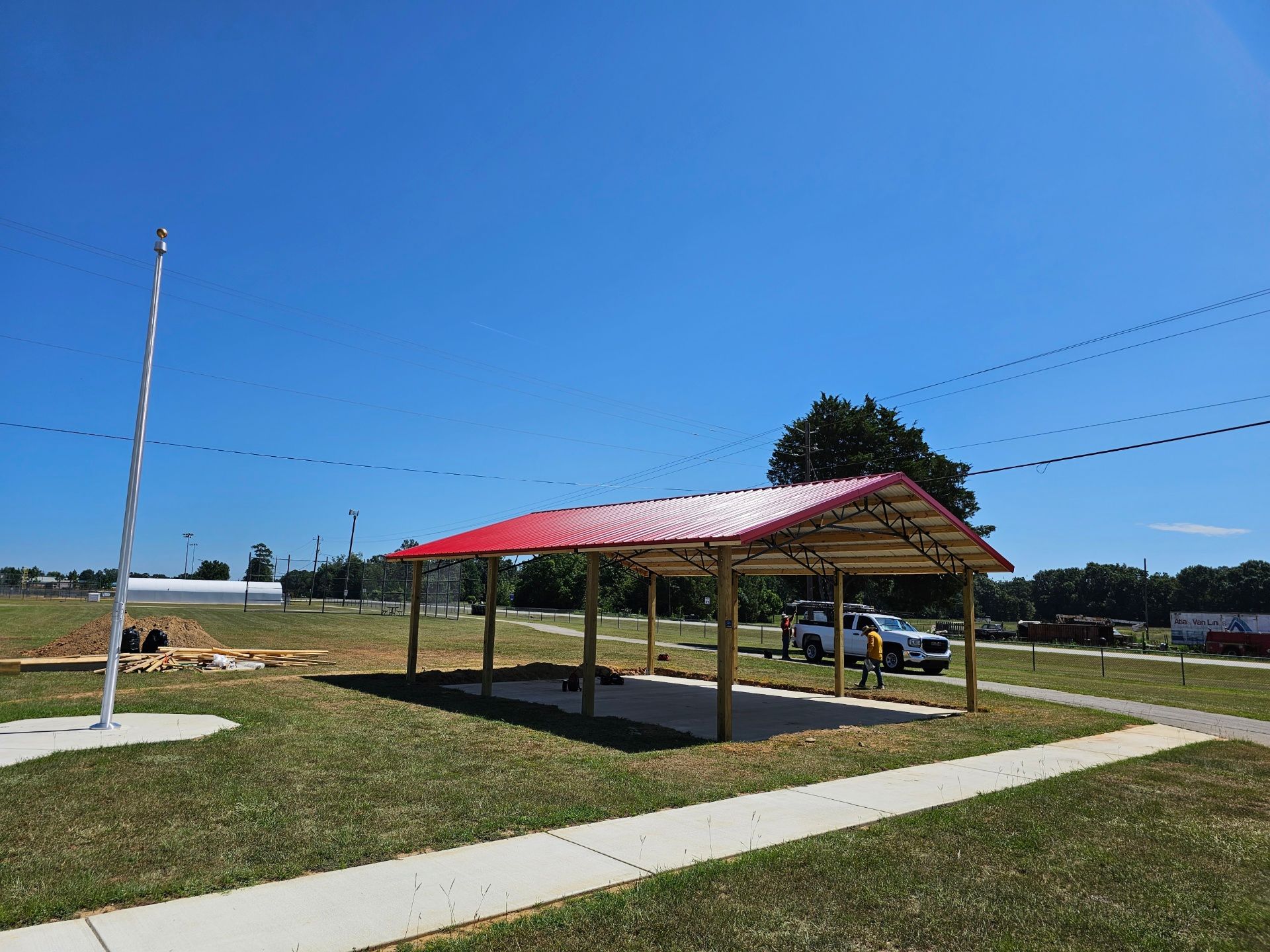 A carport with a red roof is sitting in the middle of a grassy field.