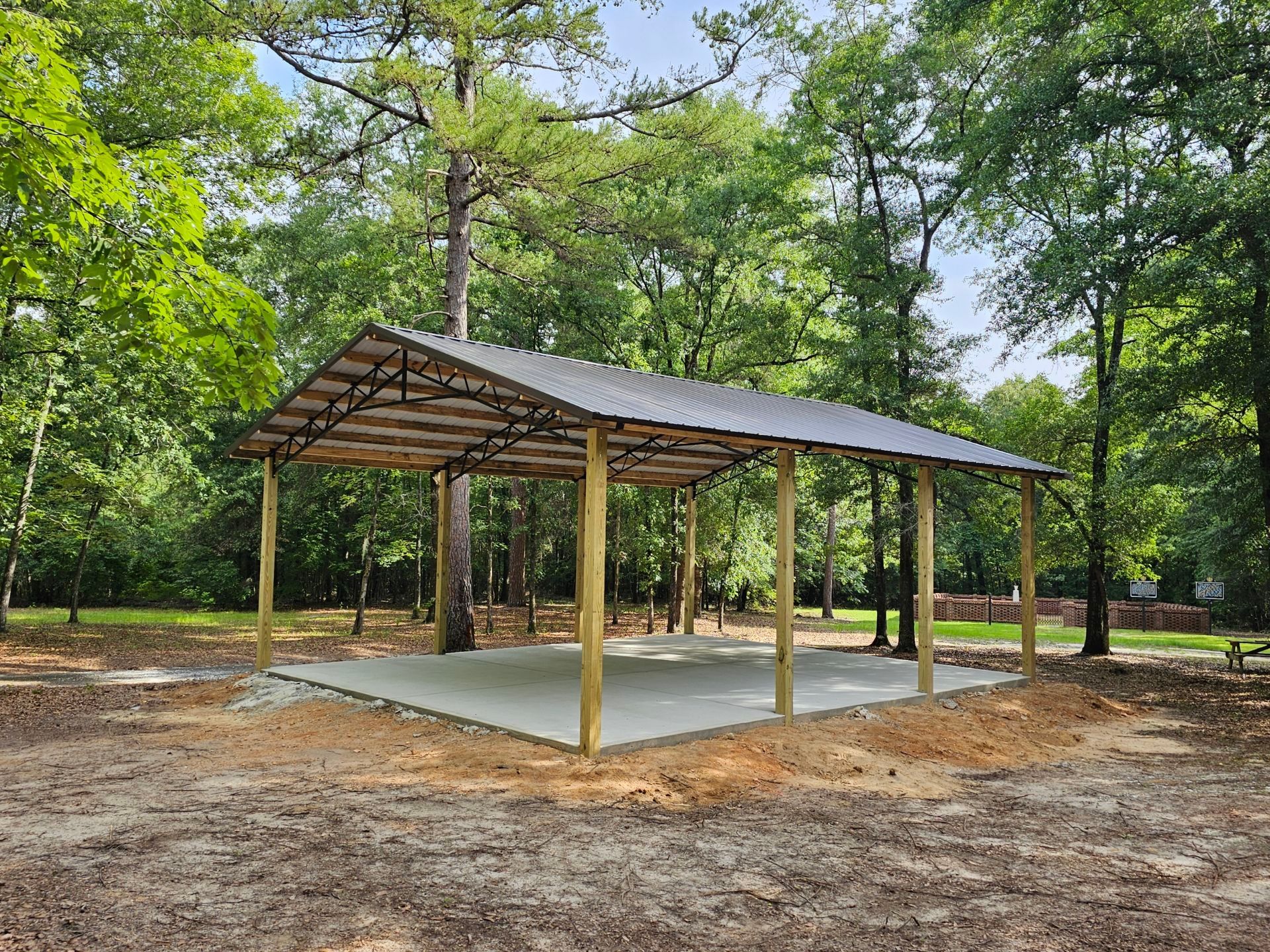 A wooden pavilion with a metal roof is surrounded by trees in a park.