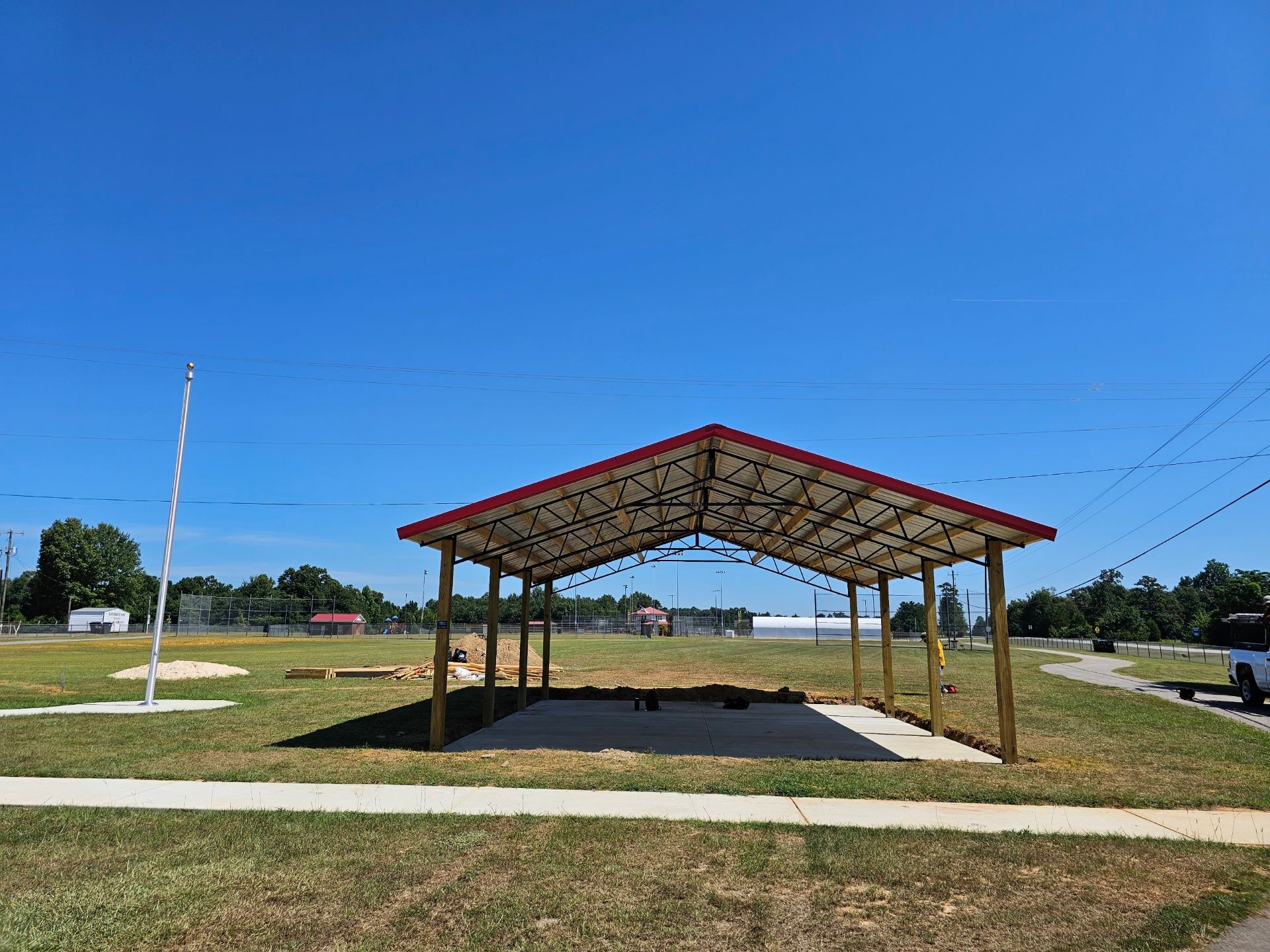 A wooden pavilion with a red roof is sitting in the middle of a grassy field.