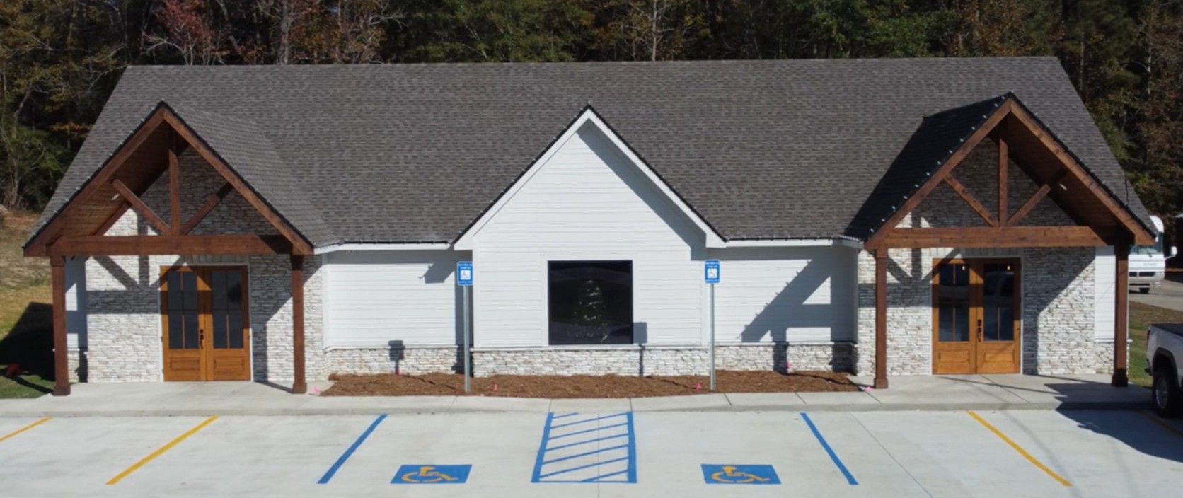 Exterior view of a white building with a dark gray roof. Entrance features brown wooden beams.