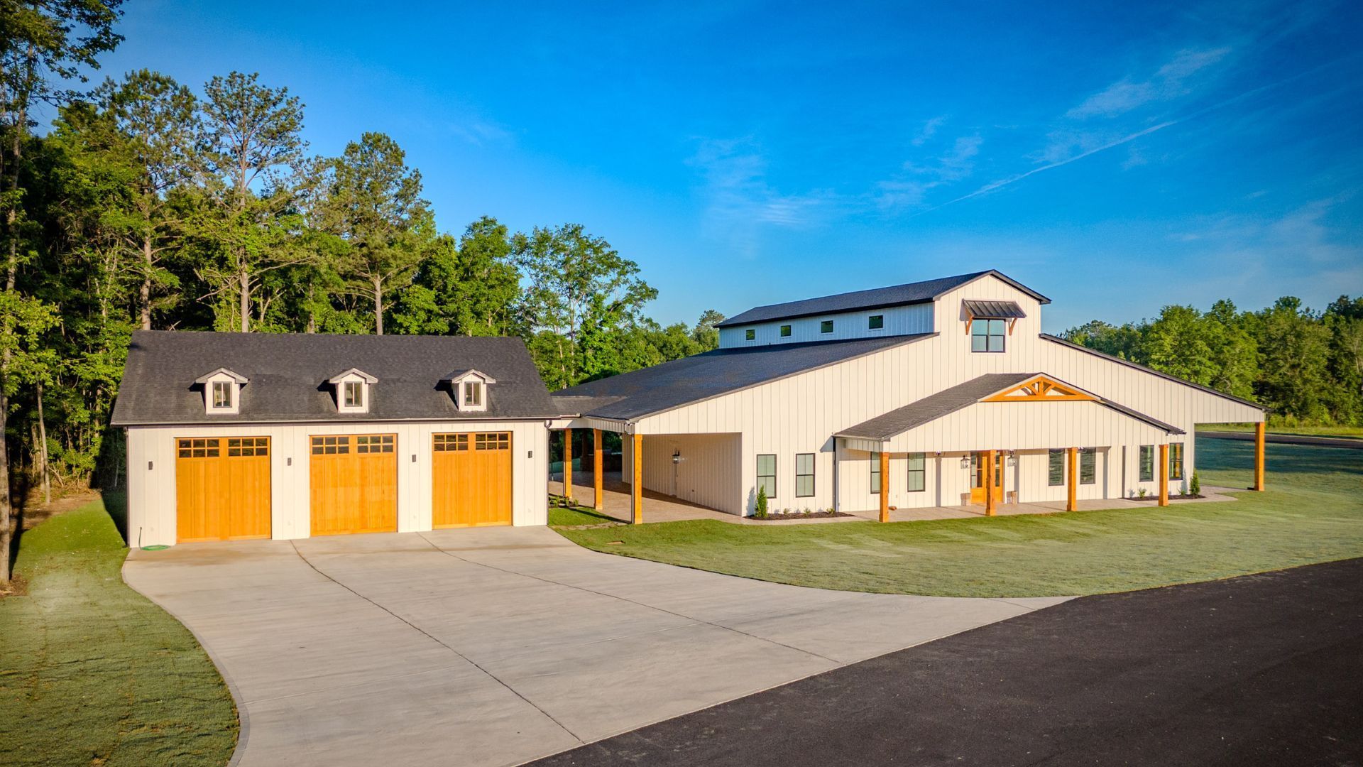 A large white house with three garage doors is sitting on top of a lush green field.