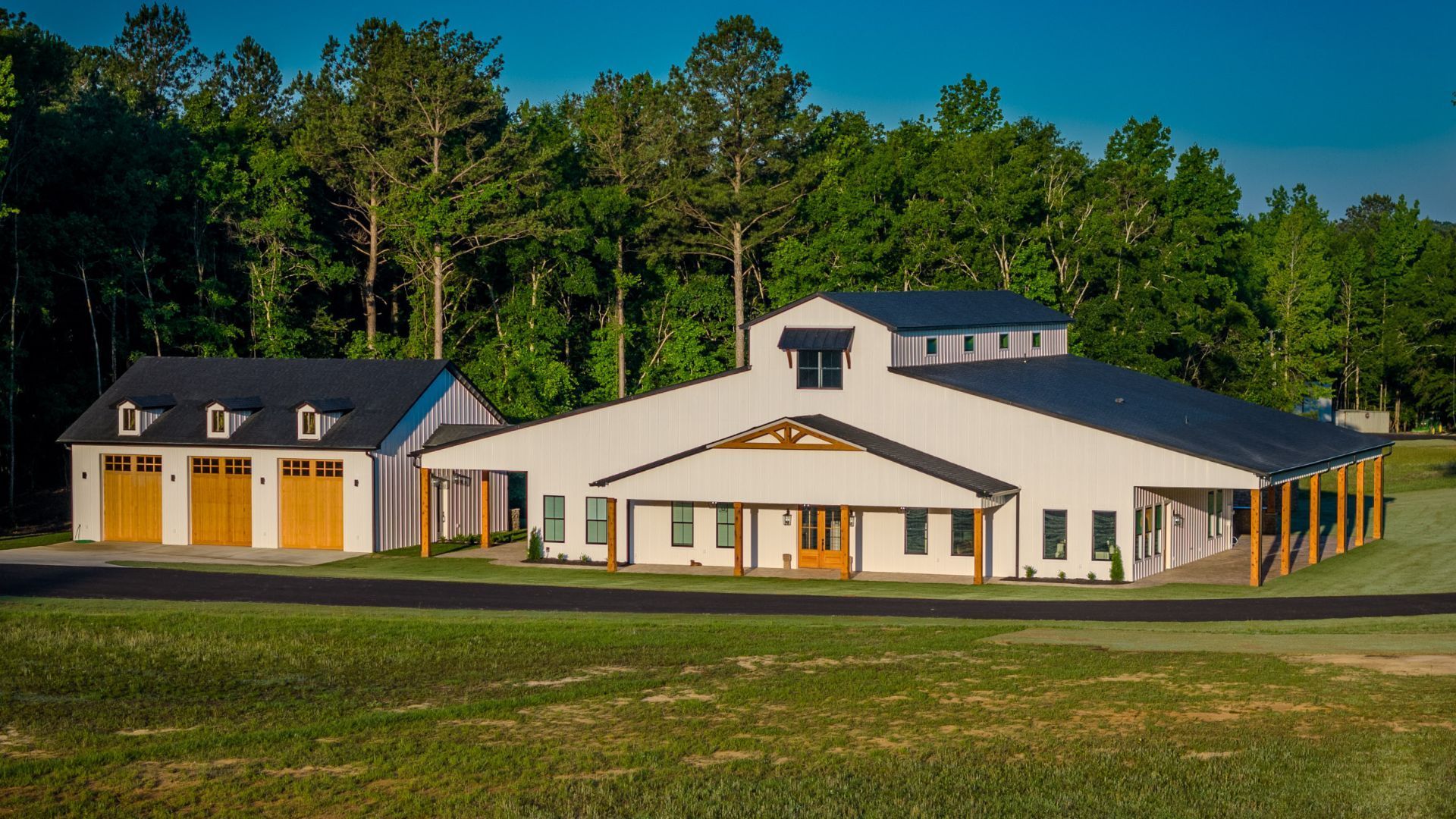 A large white building with a black roof is surrounded by trees.