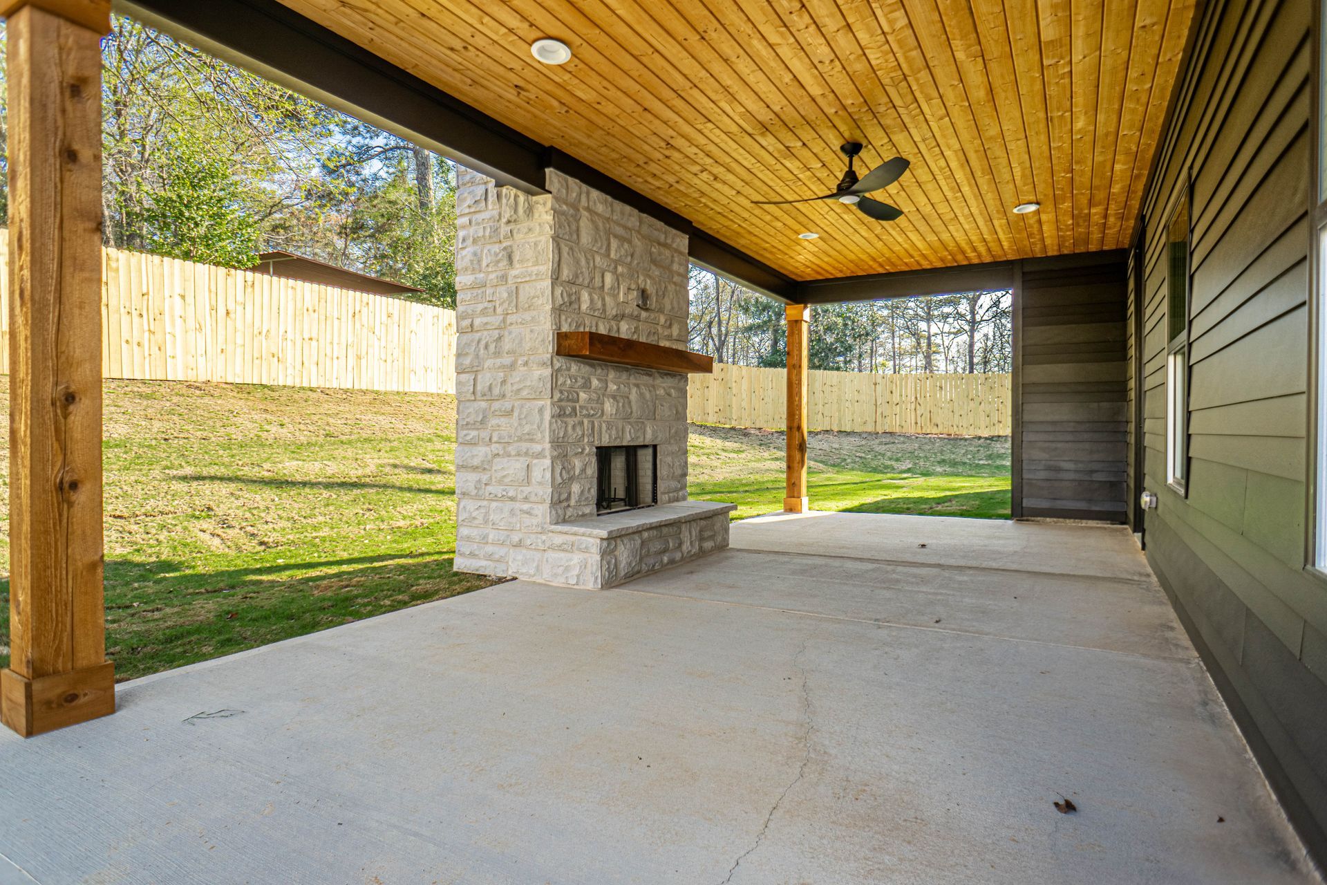 A covered patio with a fireplace and a ceiling fan.