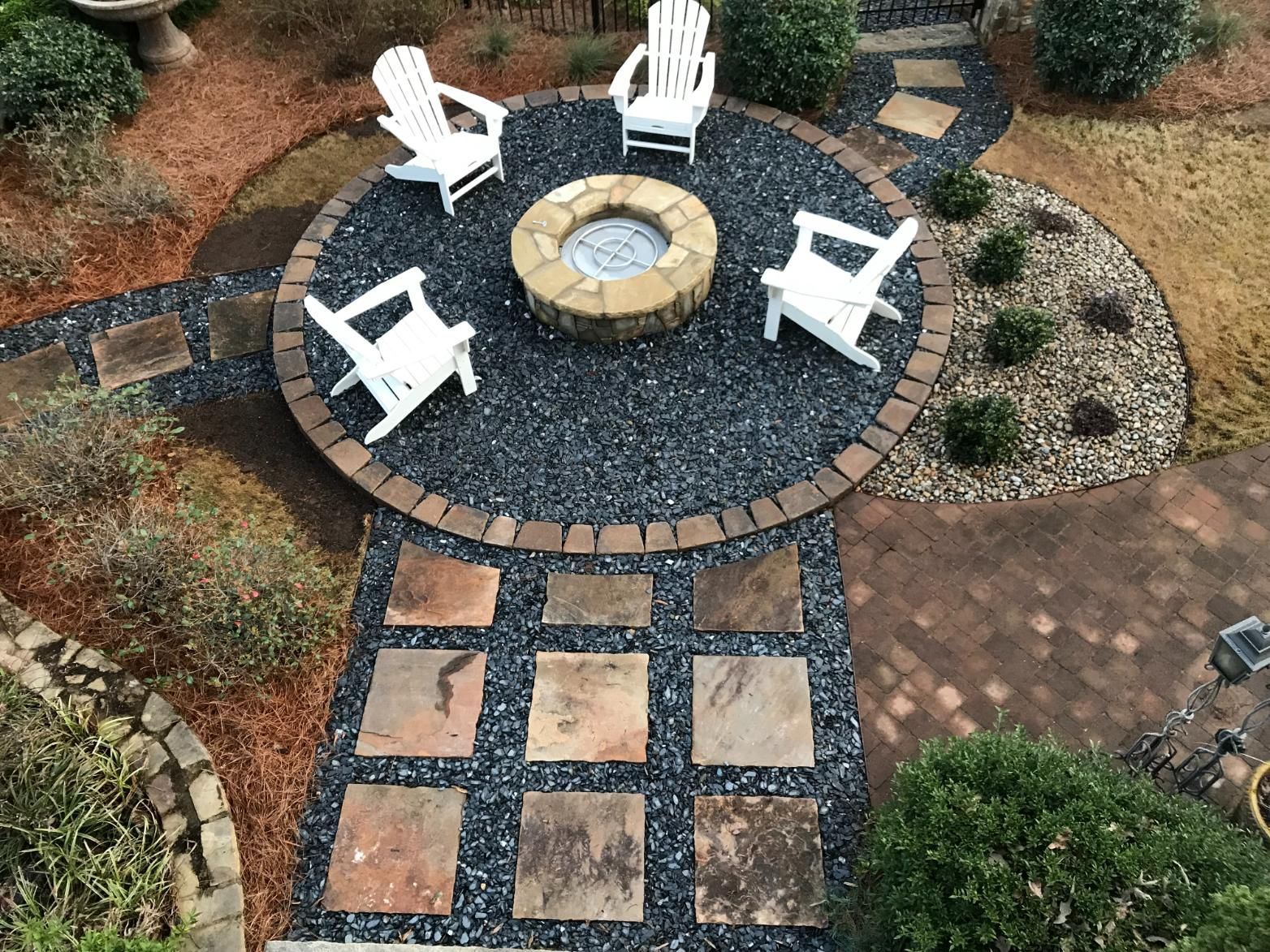 A fire pit in the middle of a patio with chairs around it.