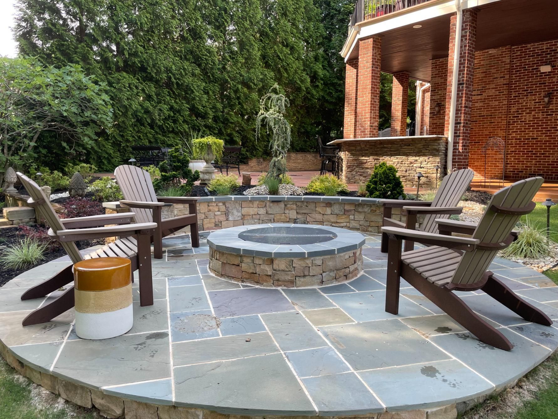 There is a fire pit in the middle of the patio with chairs around it.