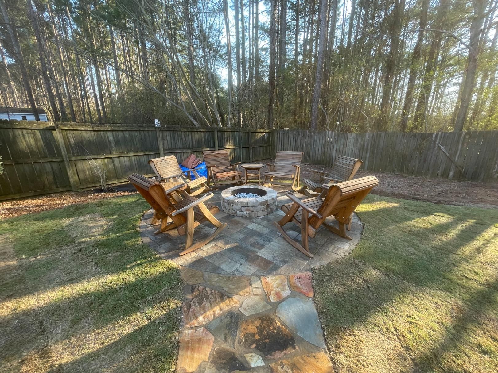 There is a fire pit in the middle of the yard with chairs around it.