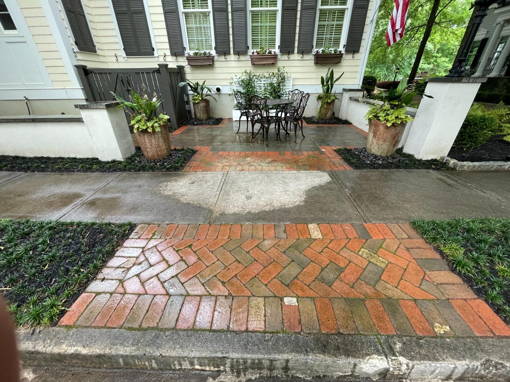 A brick walkway leading to a porch with a table and chairs.