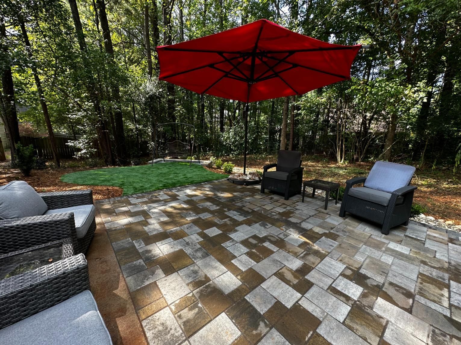 There is a red umbrella on the patio with chairs and a table.