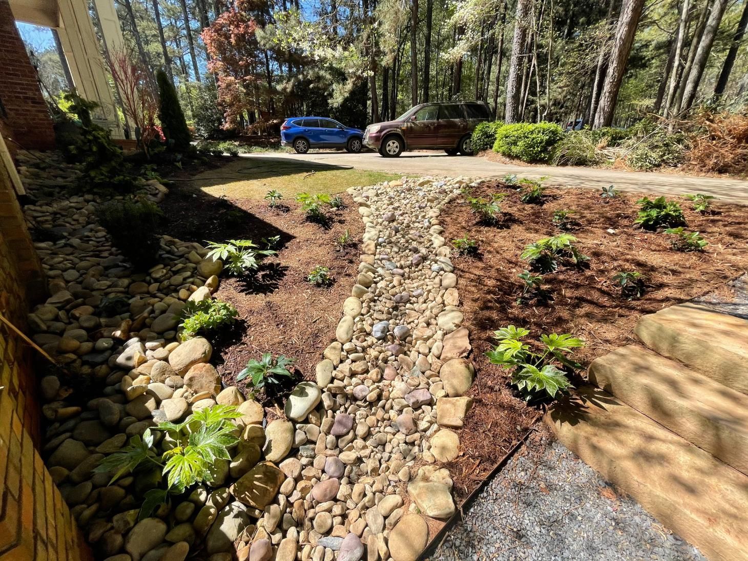 A car is parked in a driveway next to a rocky path.