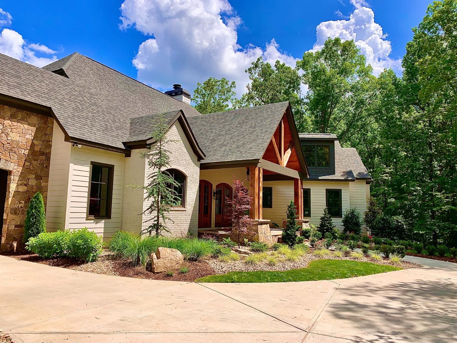A large white house with a gray roof is surrounded by trees and a driveway.