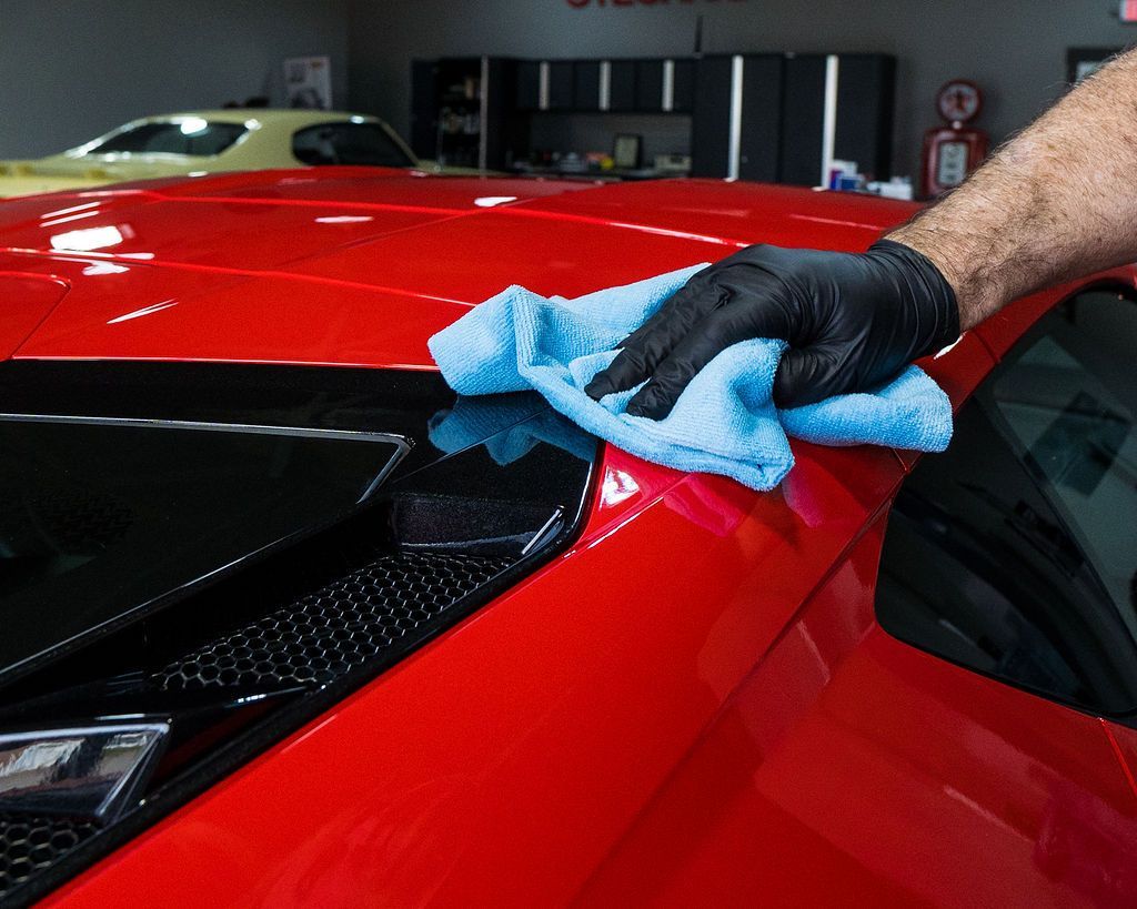 A person is cleaning a red car with a blue towel.