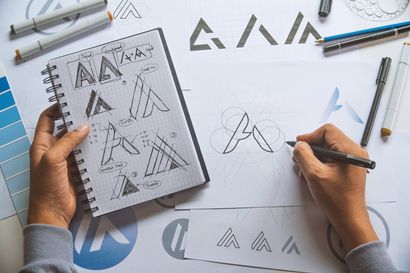 Eine Person zeichnet mit einem Stift ein Logo in ein Notizbuch.