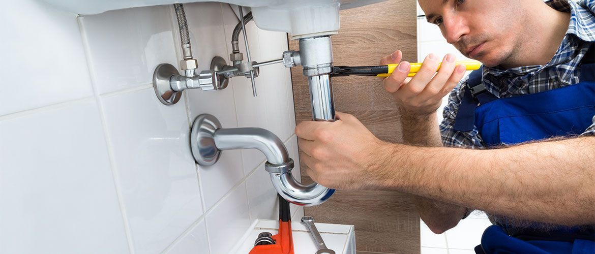 A plumber is fixing a sink in a bathroom with a wrench.