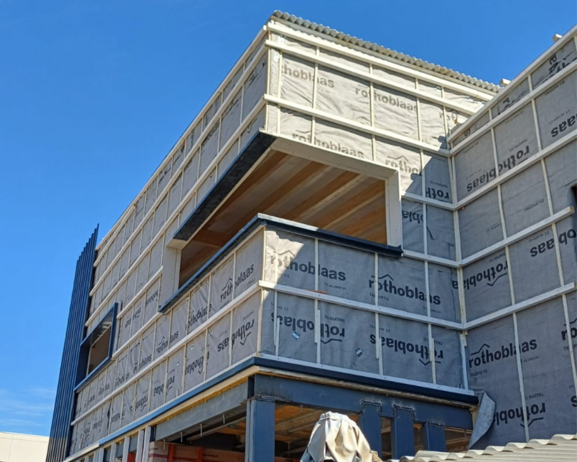 Cuatro obreros de la construcción en un tejado, trabajando en un edificio. Uno en una escalera, los demás con herramientas.