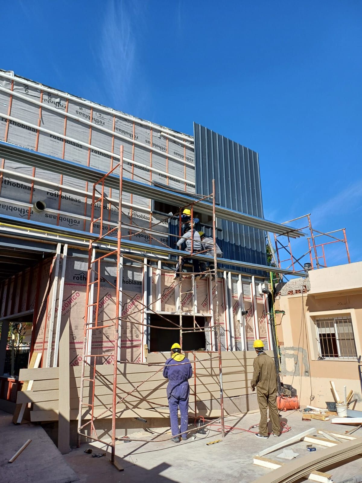 Obreros de la construcción en andamios construyendo una estructura. Cielo azul. Ropa amarilla y azul.