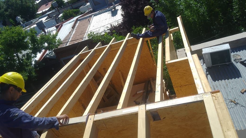 Dos trabajadores de la construcción en la azotea del edificio con estructura de madera.
