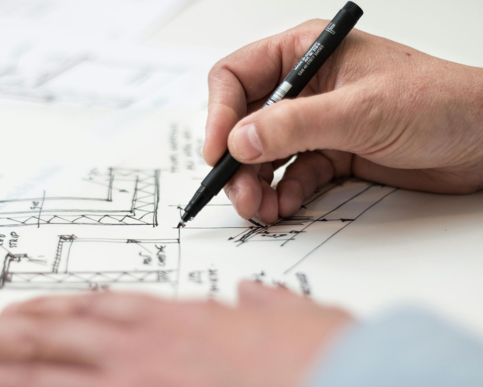 Una mano dibujando un plano con un bolígrafo negro, centrándose en los detalles arquitectónicos.