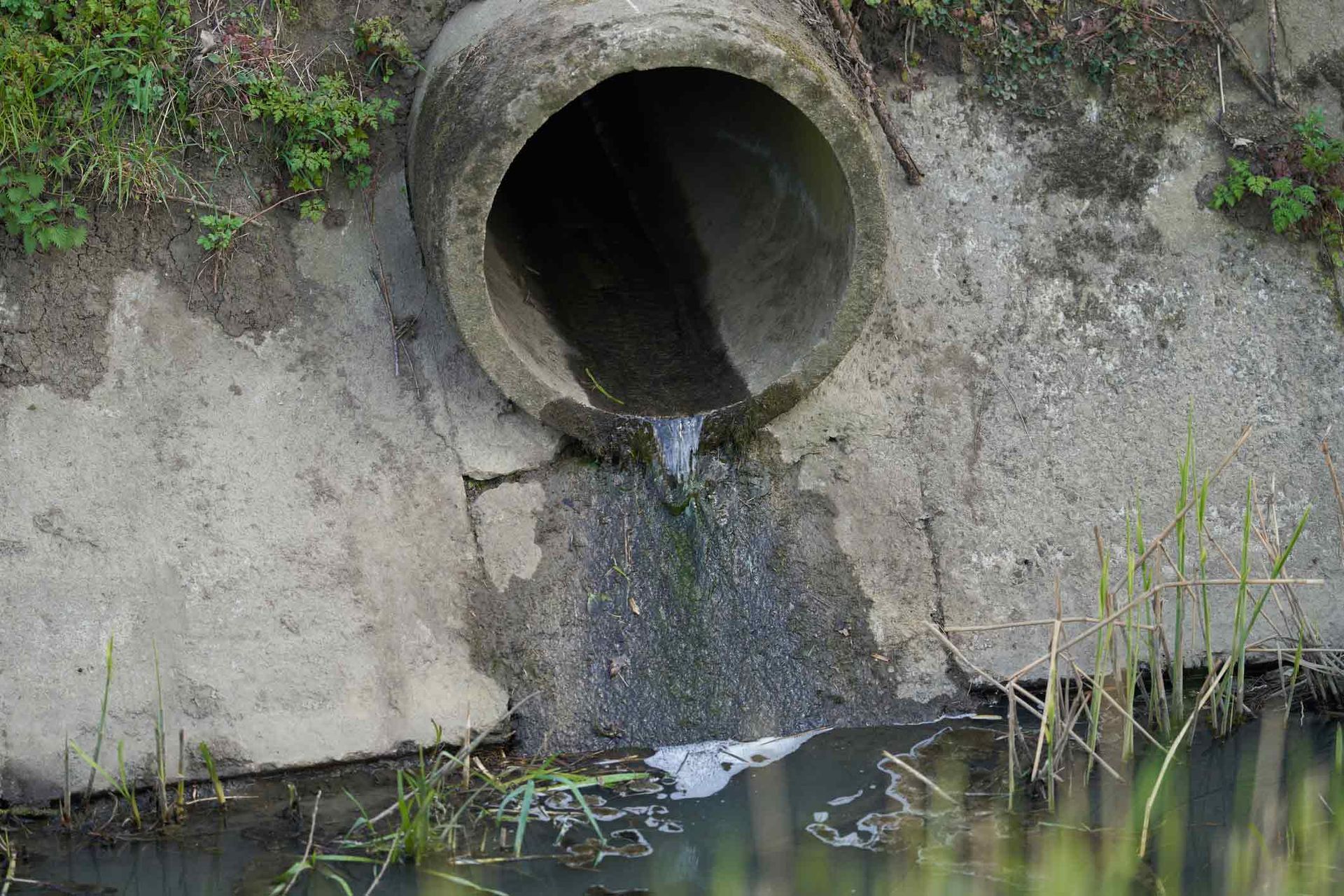 A Concrete Pipe Is Draining Water Into A River — Peoria, IL — Rooter-Matic Sewer Drain and Septic