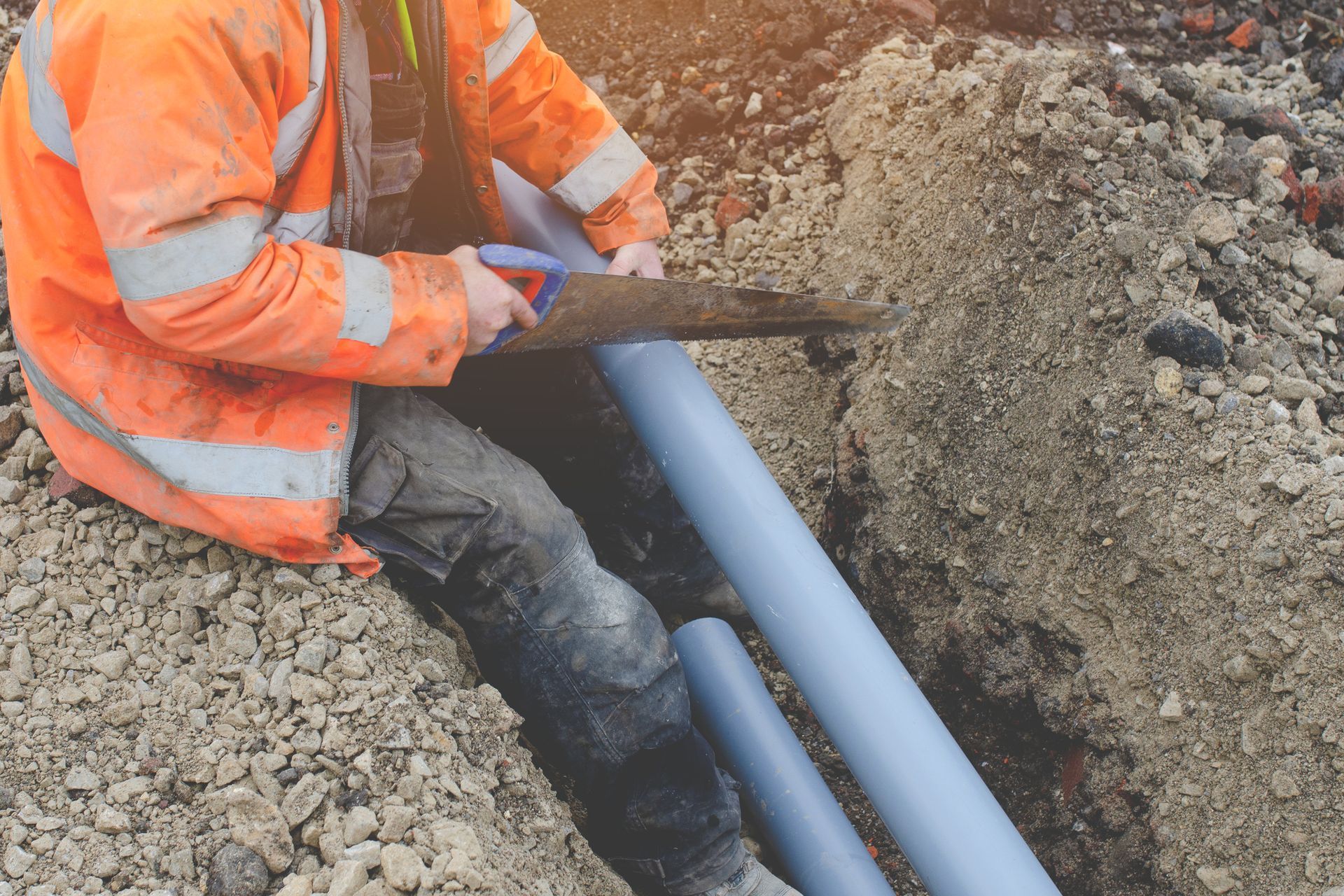 A Man is Cutting a Pipe with a Saw in the dirt — Peoria, IL — Rooter-Matic Sewer Drain and Septic