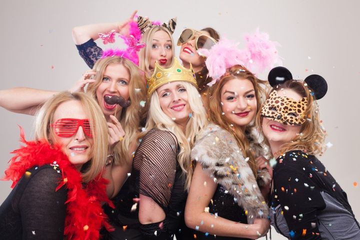 Group of people in colorful costumes and wigs posing closely together with playful expressions