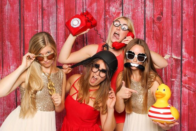 Five women in red and white outfits posing playfully with props against a pink wooden backdrop