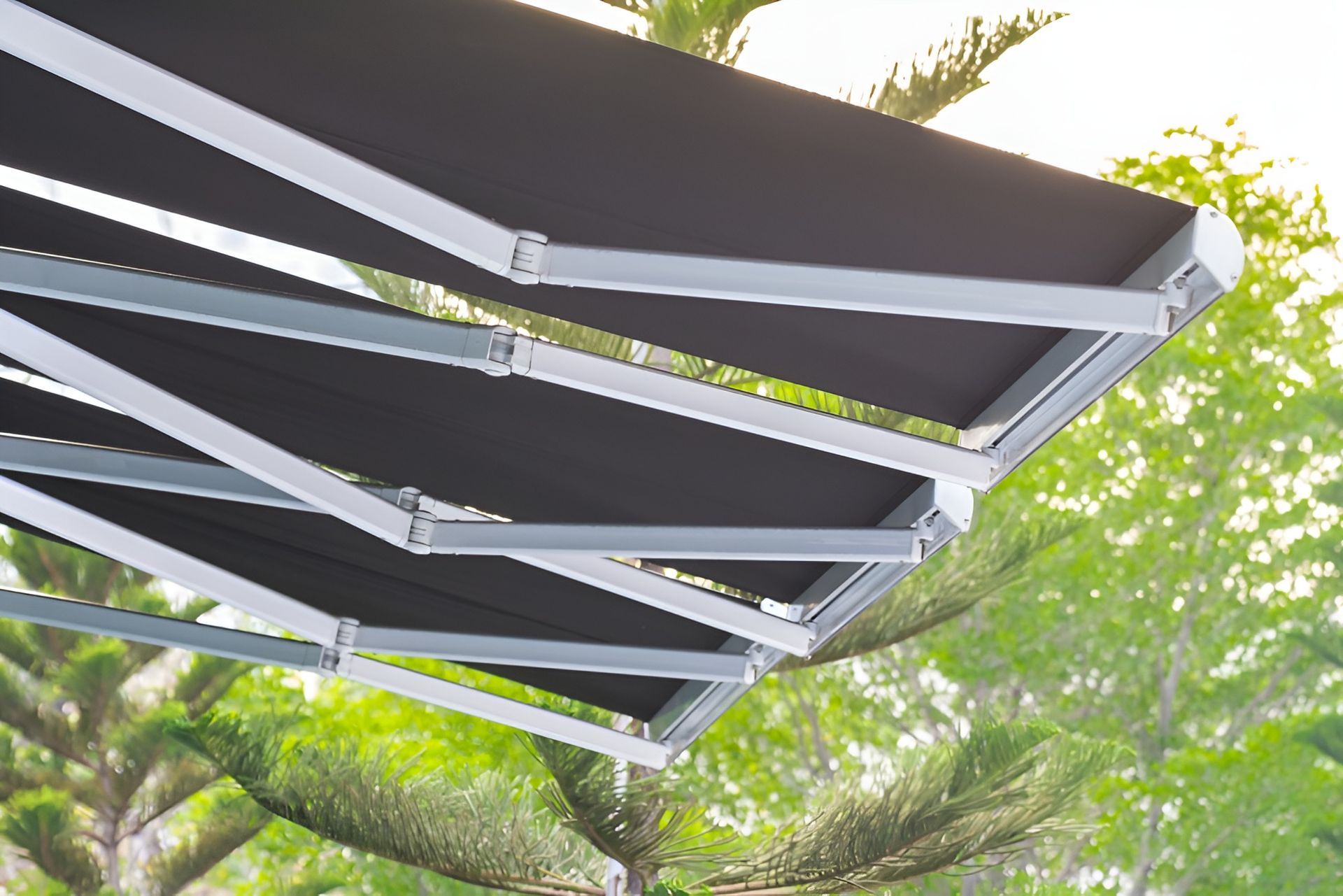 Black Retractable Awning with Silver Frame, Against Green Trees — BlindDESIGN in Byron Bay, NSW