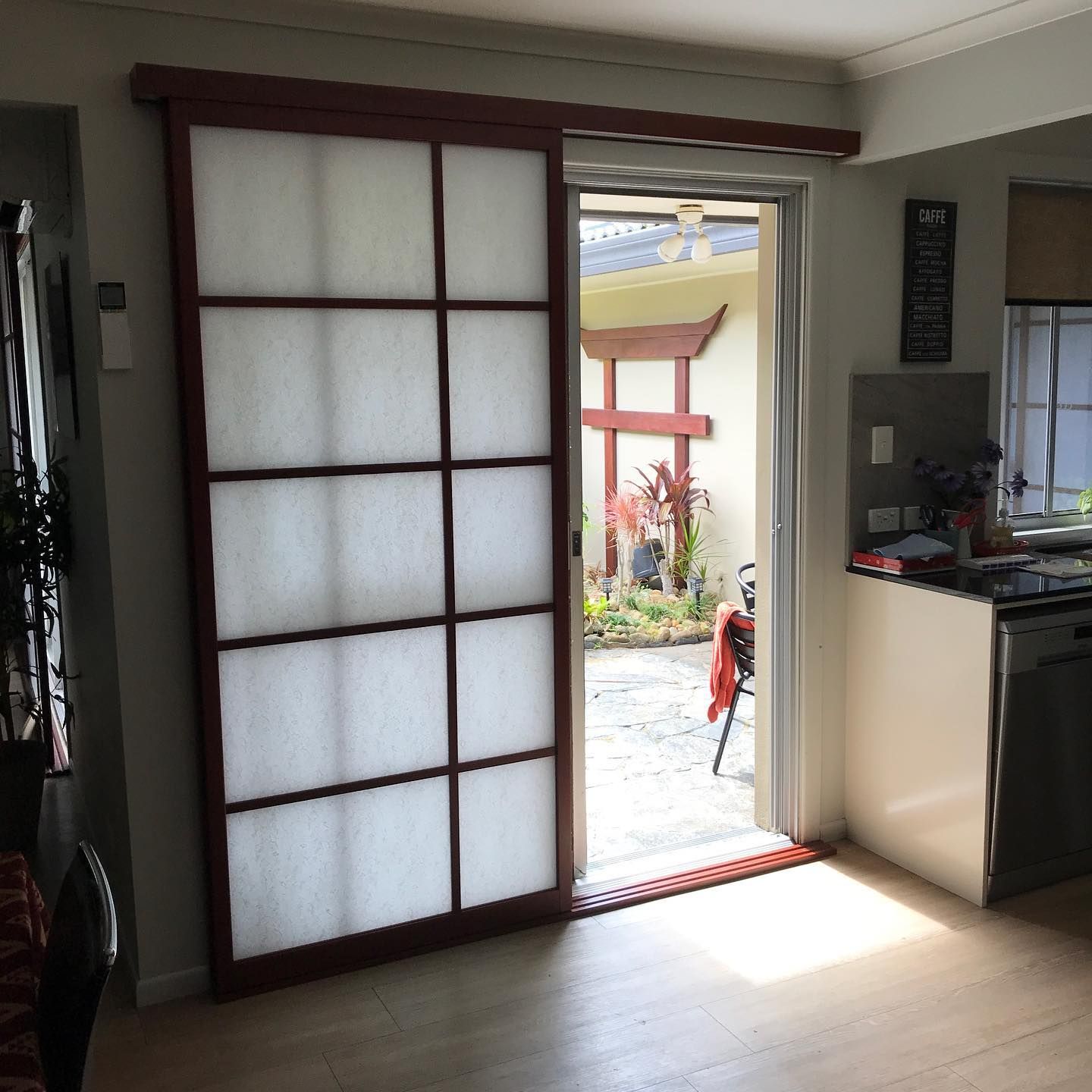 Sliding Shoji screen door, red frame, white panels, open to a garden with a red structure — BlindDESIGN in Byron Bay, NSW