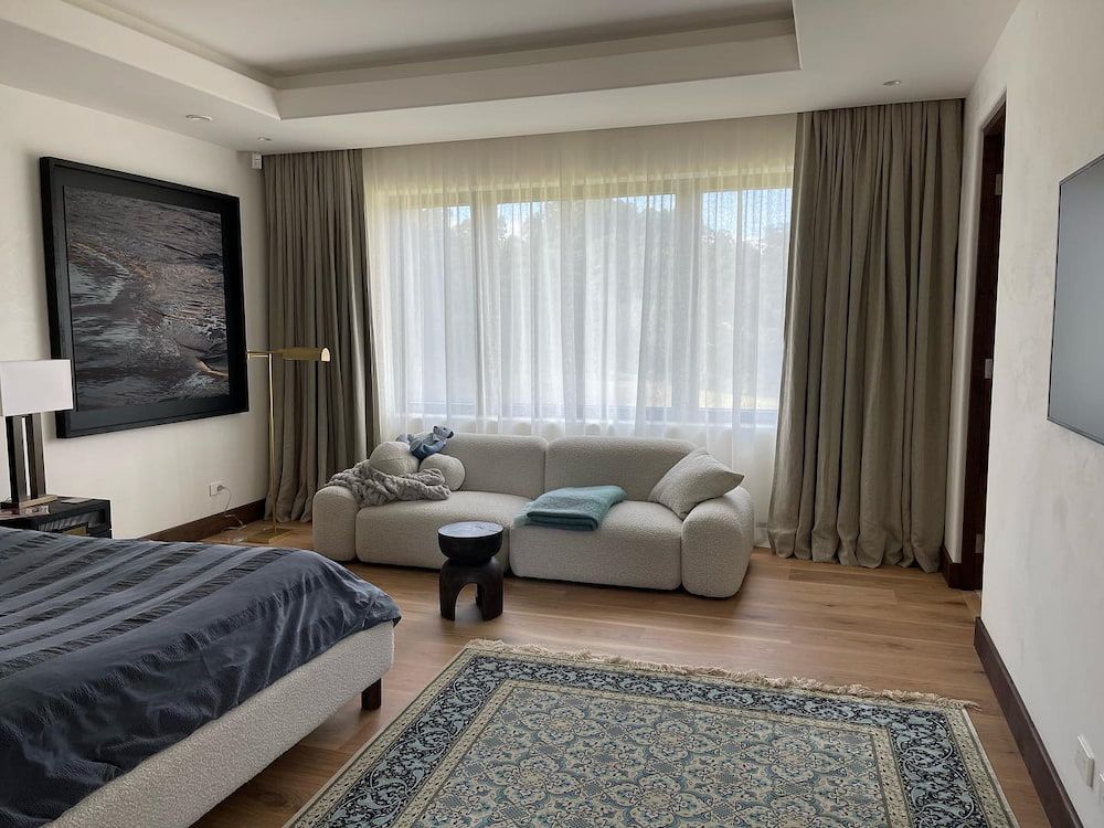 Bedroom With a White Sofa, Large Window With Curtains, Artwork, and a Bed With a Blue Comforter — BlindDESIGN in Lismore, NSW