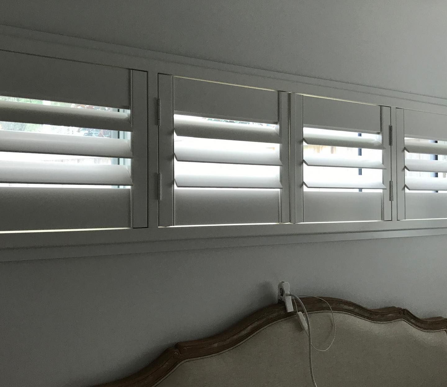 White Shutters on a Window Above an Ornate Bed Headboard, Partially Open for Light — BlindDESIGN in Ballina, NSW