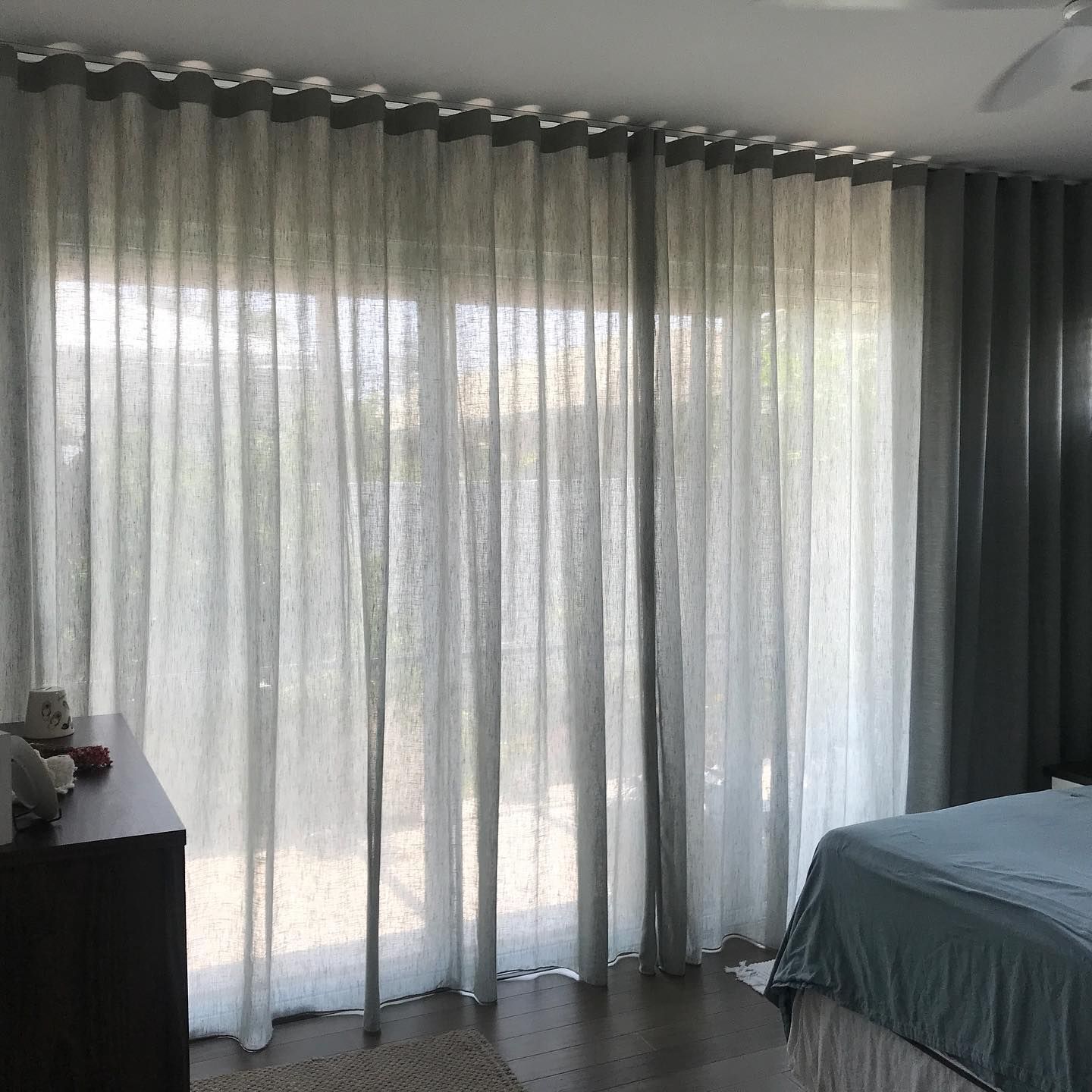 Bedroom With Sheer Light Gray Curtains Covering a Large Window — BlindDESIGN in Byron Bay, NSW
