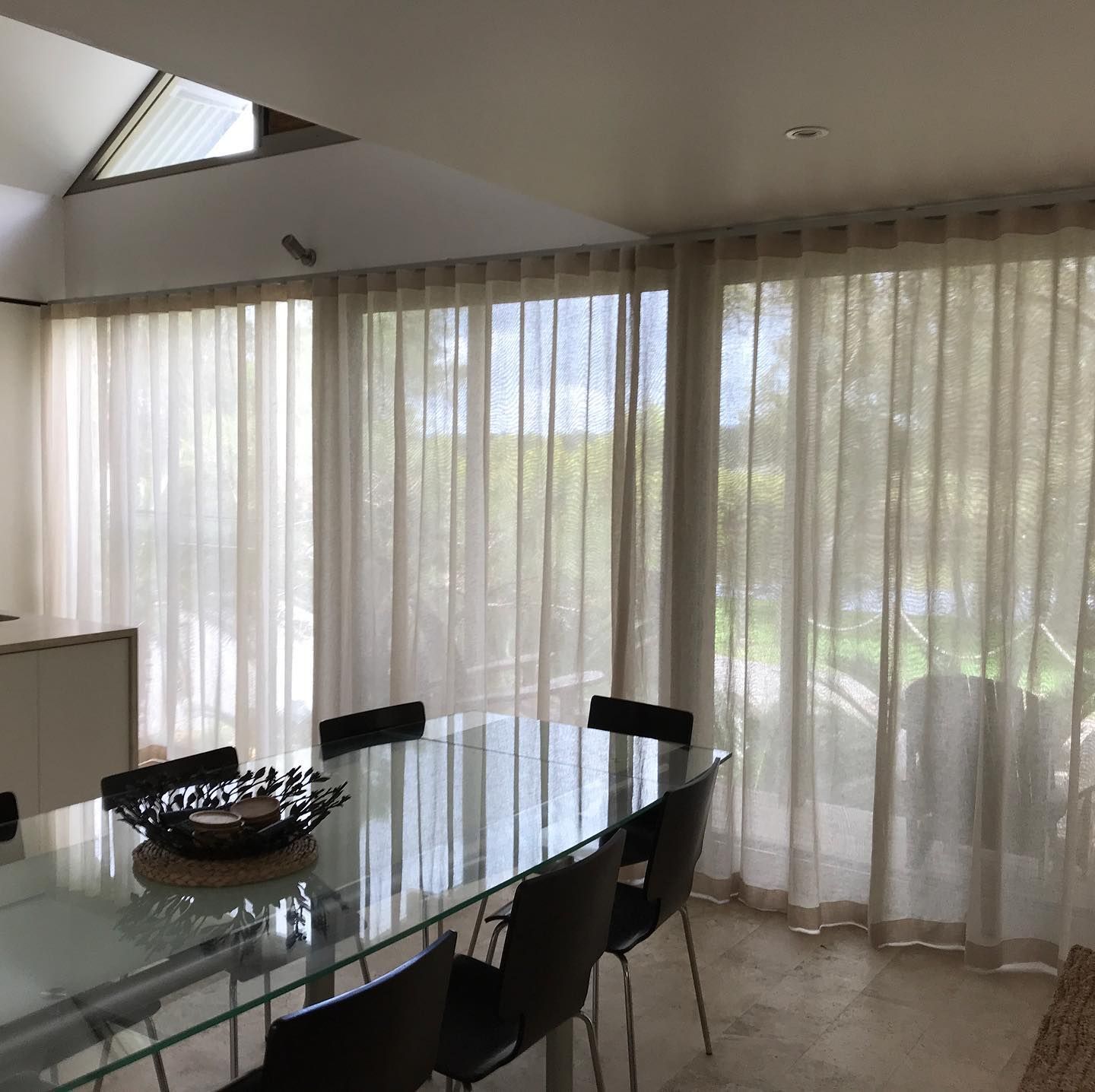 Dining Room With a Glass Table, Black Chairs, and Sheer Beige Curtains — BlindDESIGN in Byron Bay, NSW