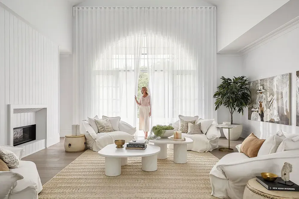 White Living Room With Arched Window, Sheer Curtains, and Woman Looking Outside — BlindDESIGN in Byron Bay, NSW