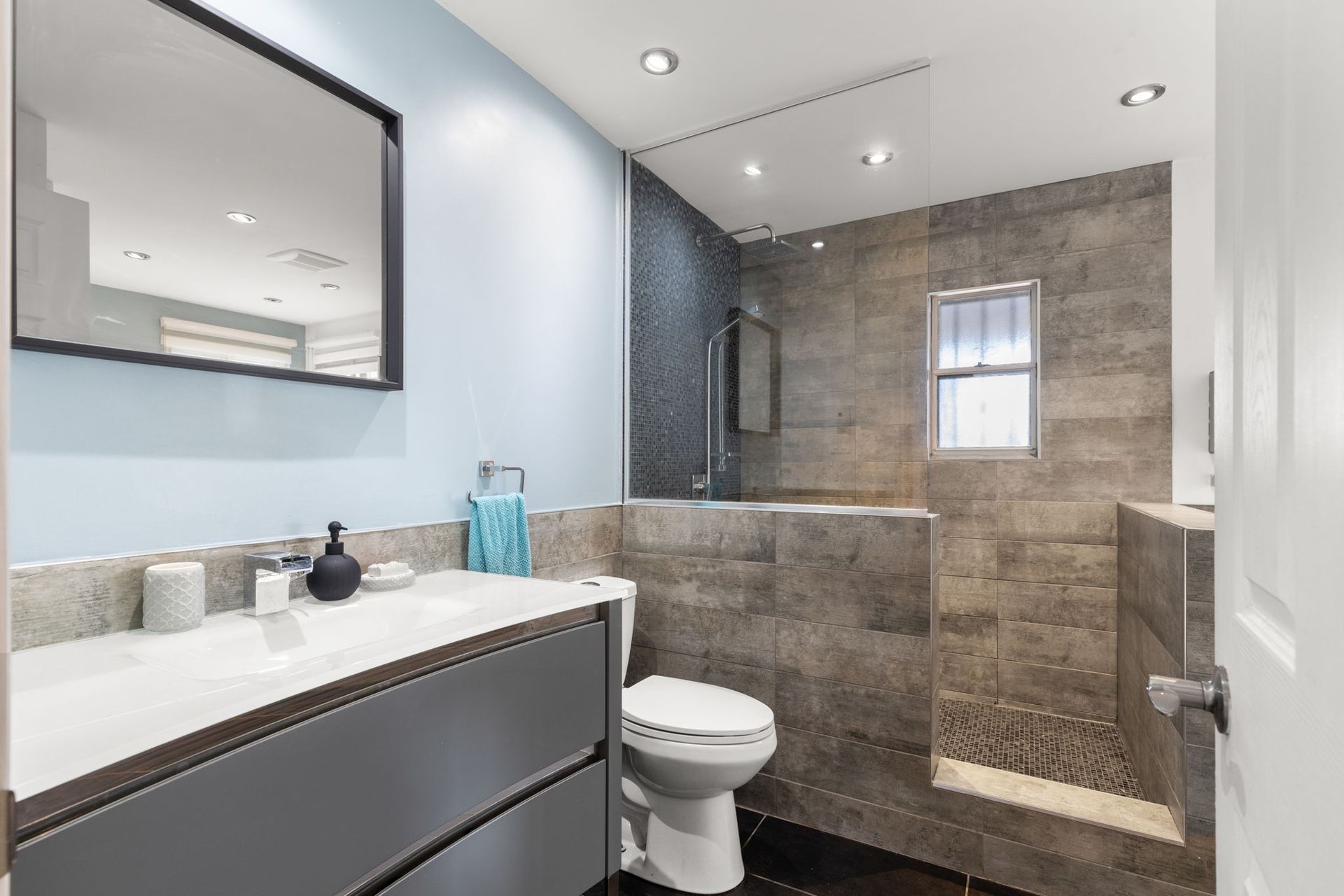 Salle de bains moderne avec murs bleus, meuble-lavabo gris et douche carrelée.