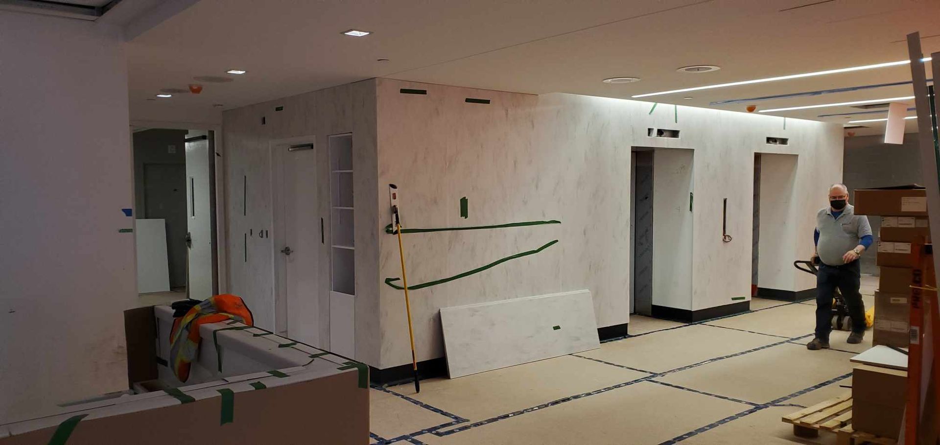 Chantier de construction avec une personne se dirigeant vers deux ascenseurs. Intérieur d'un bâtiment.