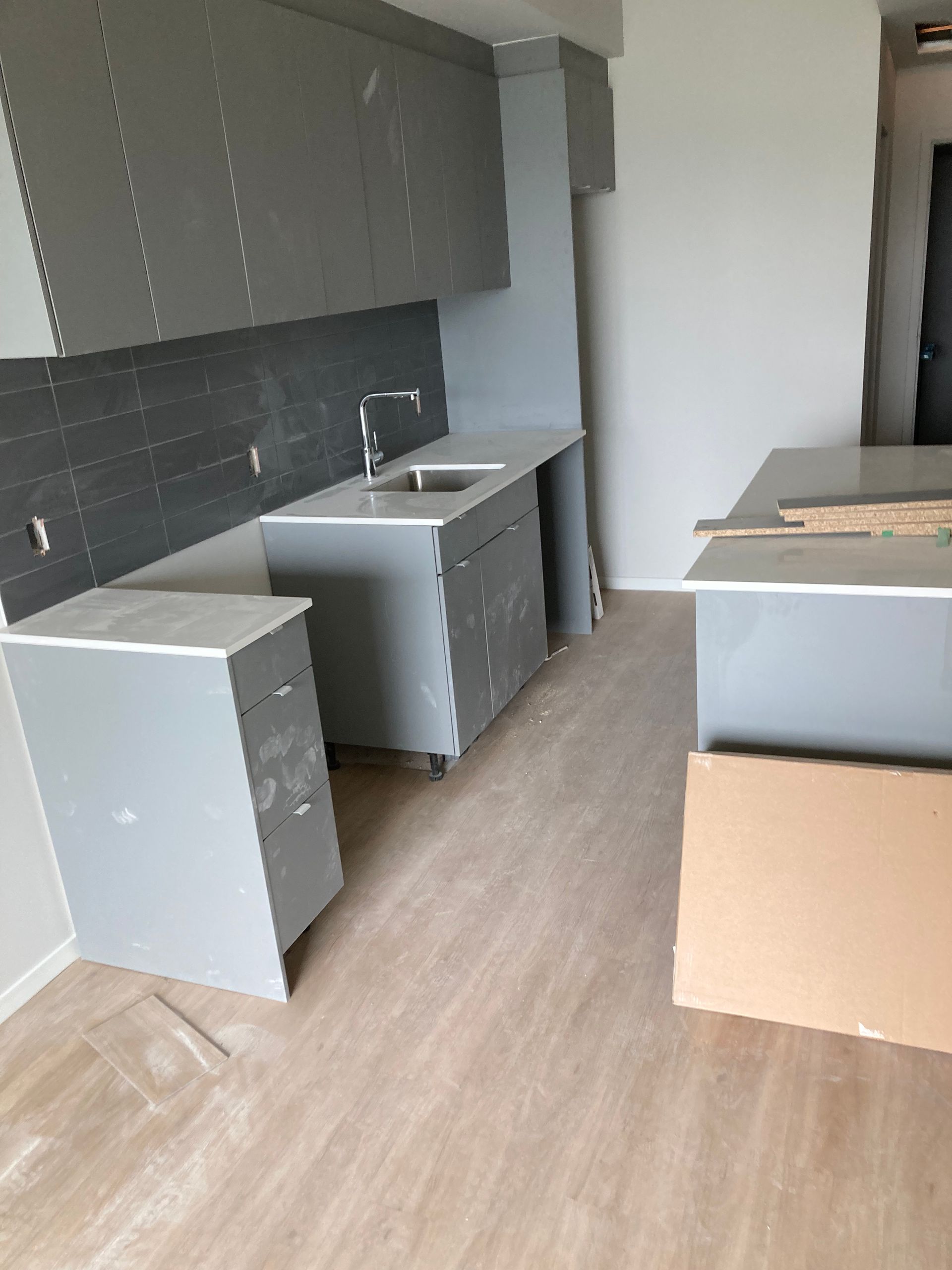 Installation en cours des meubles de cuisine gris, du plan de travail et de la crédence carrelée.