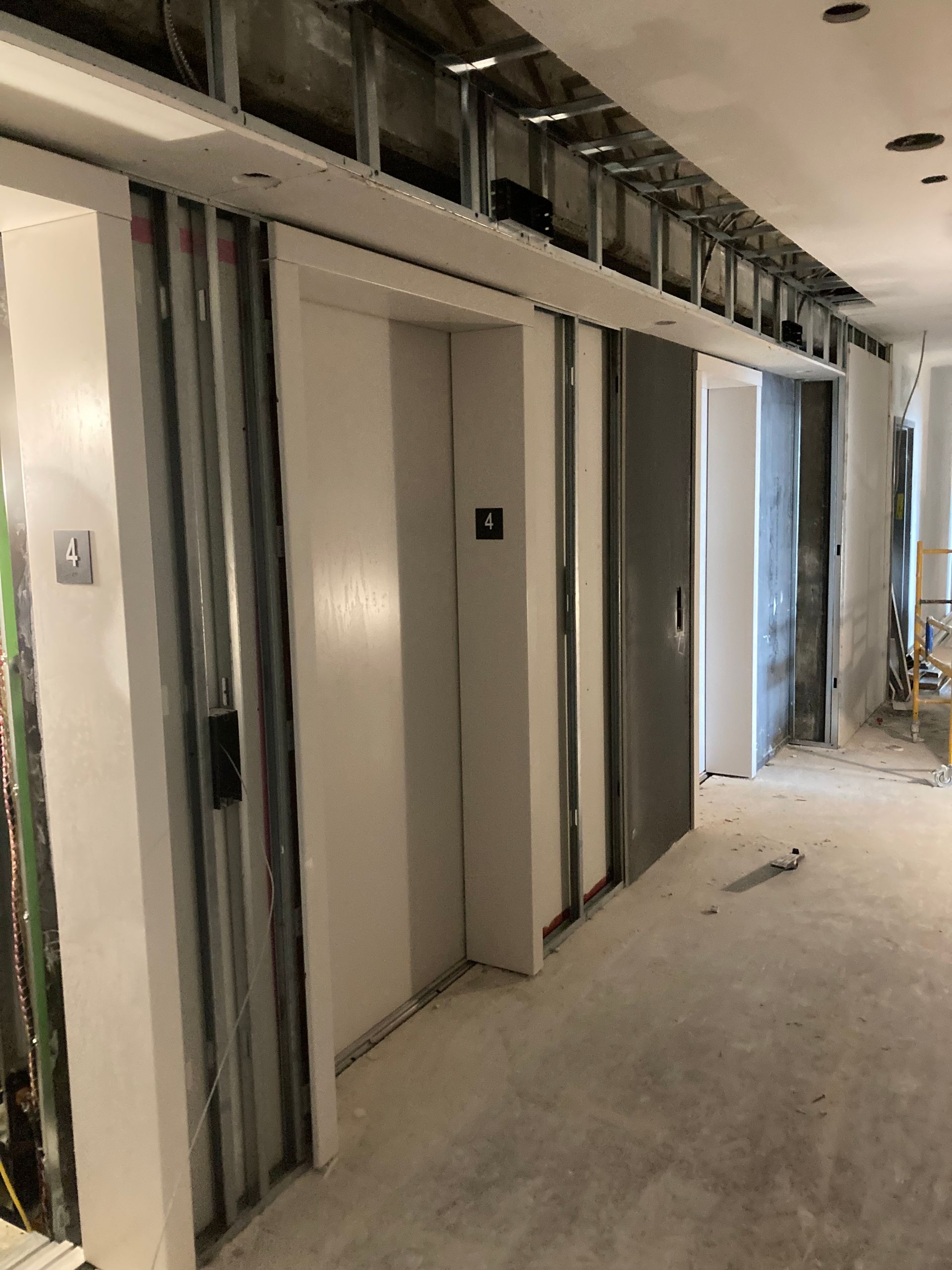 Couloir en construction avec porte d'ascenseur et structure métallique.