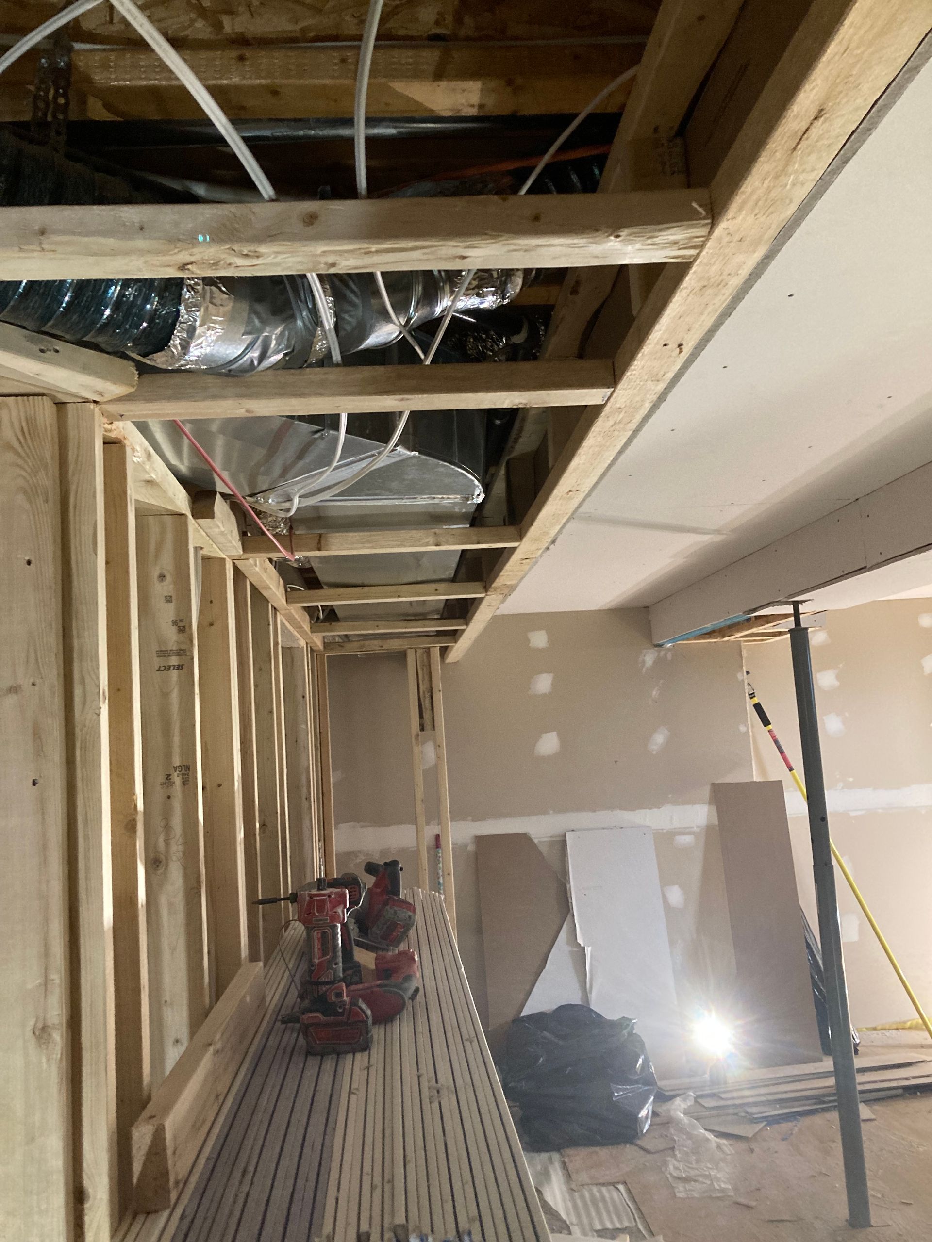 Chantier de construction intérieur avec charpente apparente, conduits de ventilation et outils.