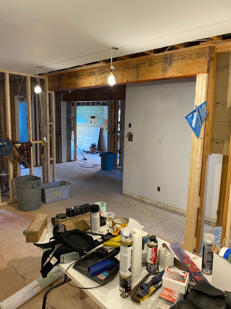 Pièce intérieure en rénovation, charpente apparente, outils sur une table, vue d'une porte menant à une autre pièce.