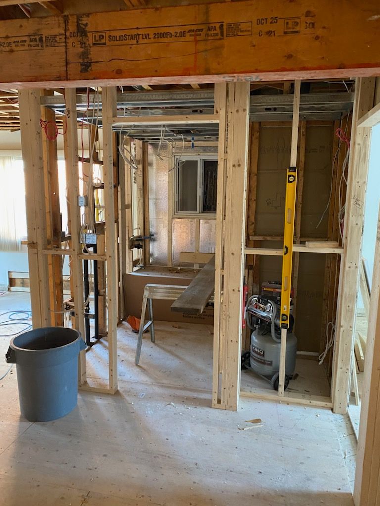 Intérieur en travaux ; charpente en bois, tuyaux et compteur de gaz visibles. Seau bleu au sol.