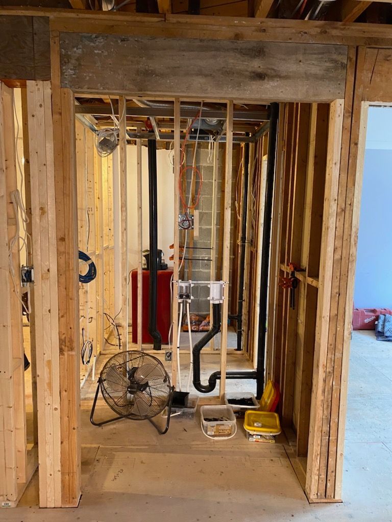 Aménagement intérieur avec charpente apparente, tuyauterie et câblage électrique. Un ventilateur est posé au sol.