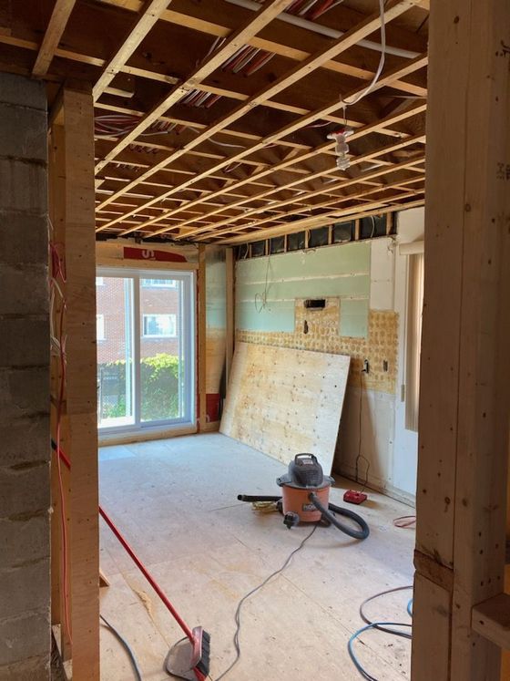 Pièce en travaux : solives de plafond apparentes, cloisons sèches, porte coulissante en verre et aspirateur.