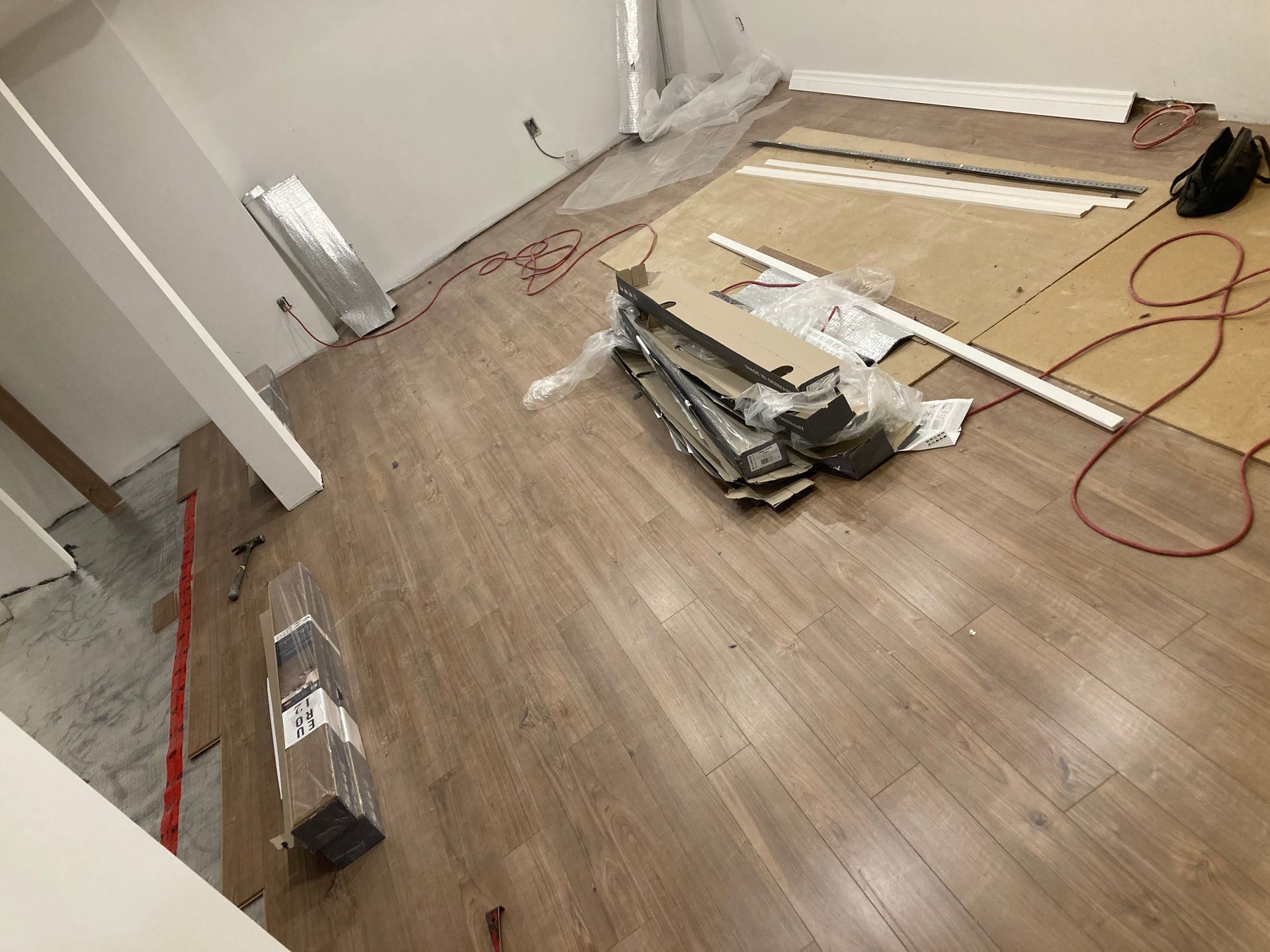 Pièce avec revêtement de sol imitation bois, lames empilées, moulures et outils ; murs non finis.
