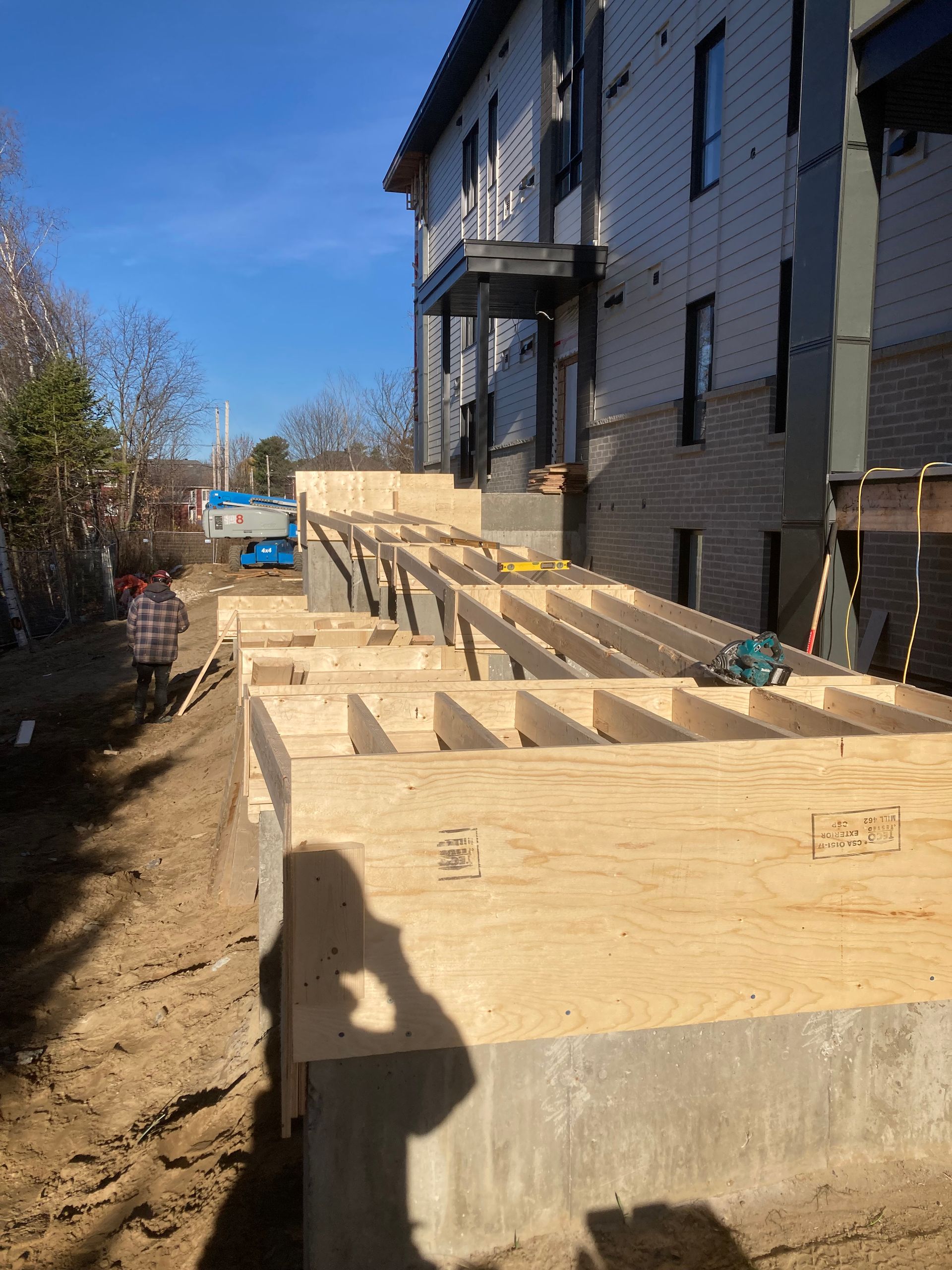 Chantier : une plateforme à ossature bois est en construction à côté d'un immeuble de plusieurs étages. Journée ensoleillée.