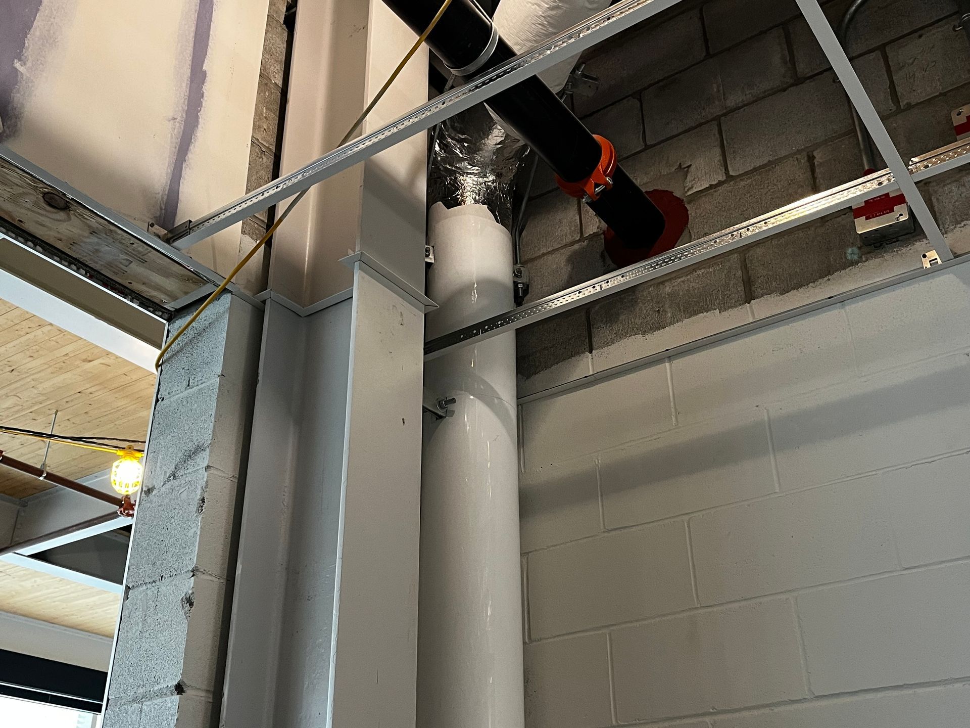 Intérieur d'un chantier avec tuyauterie apparente et mur de briques. Plafond partiellement installé.