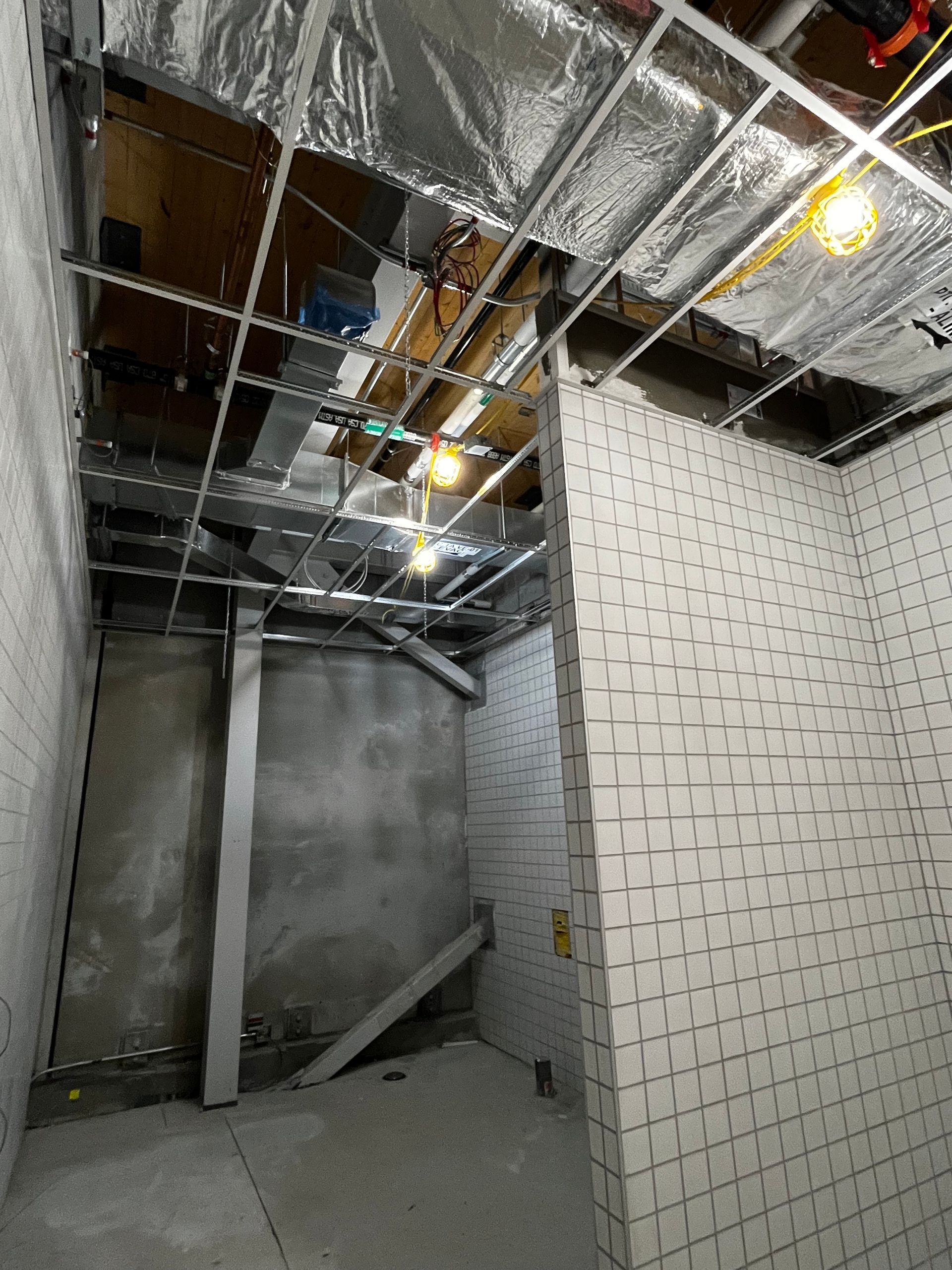 Intérieur en travaux : plafond à ossature apparente, murs en béton, pièce inachevée avec éclairage.